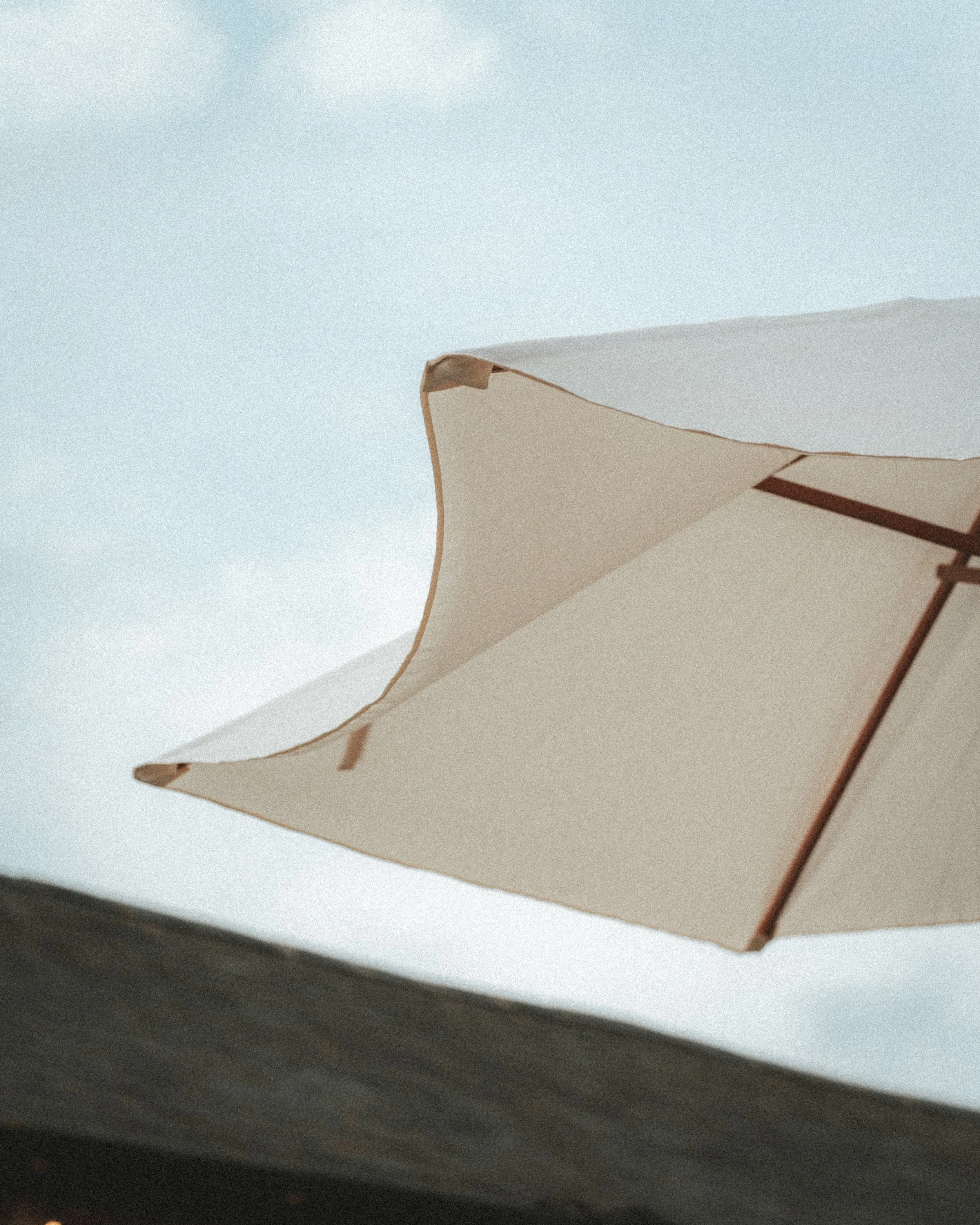 Close-up of a beige umbrella with a decorative trim, set against a clear blue sky.