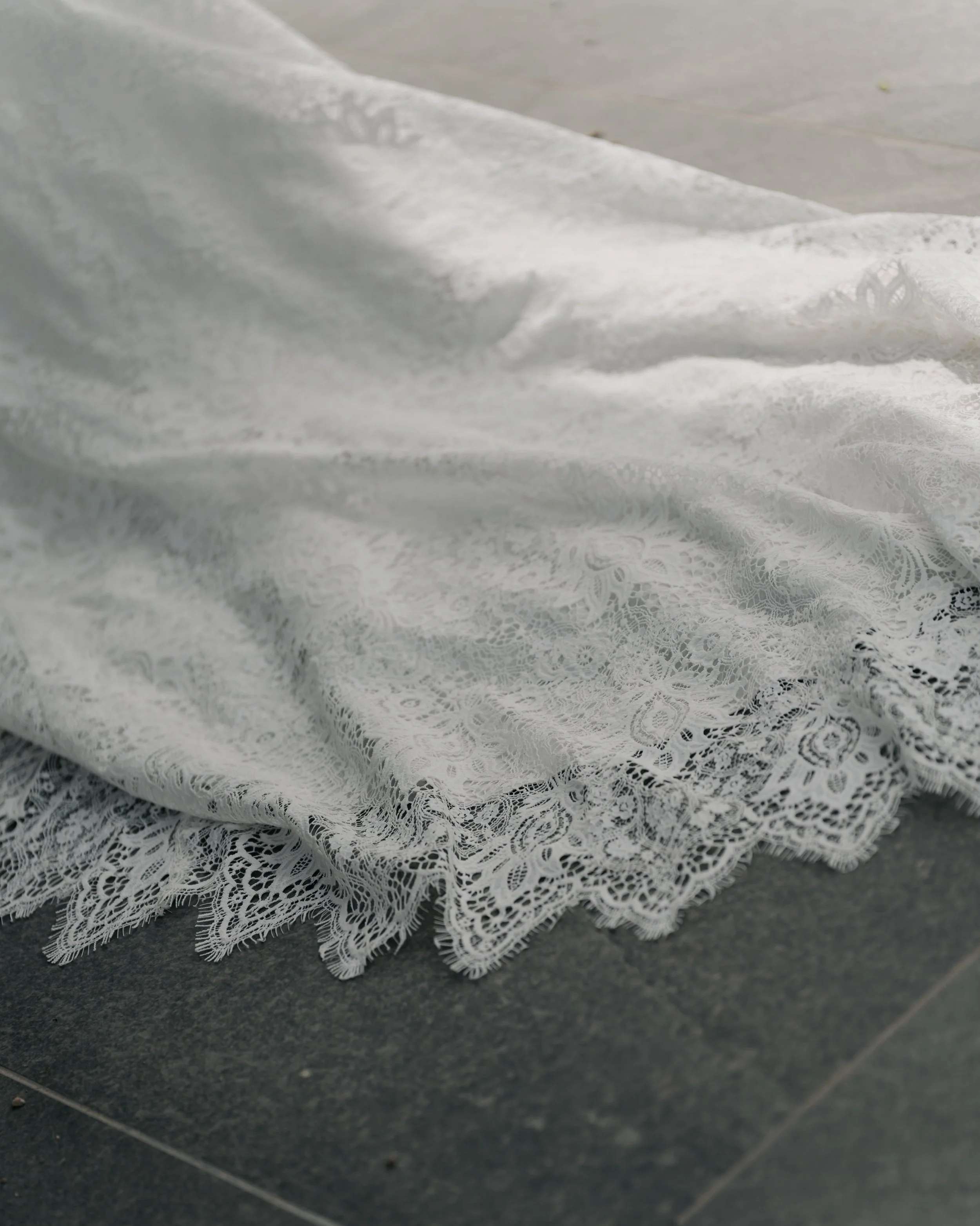 Close-up of white lace fabric with floral patterns, draped over a dark tiled surface.
