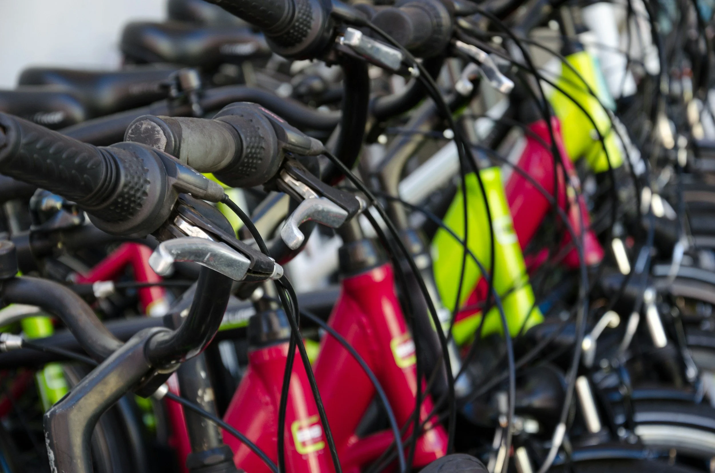 Close-up of several parked bicycles with black handlebars and gear shifters, some with bright pink and yellow frames.
