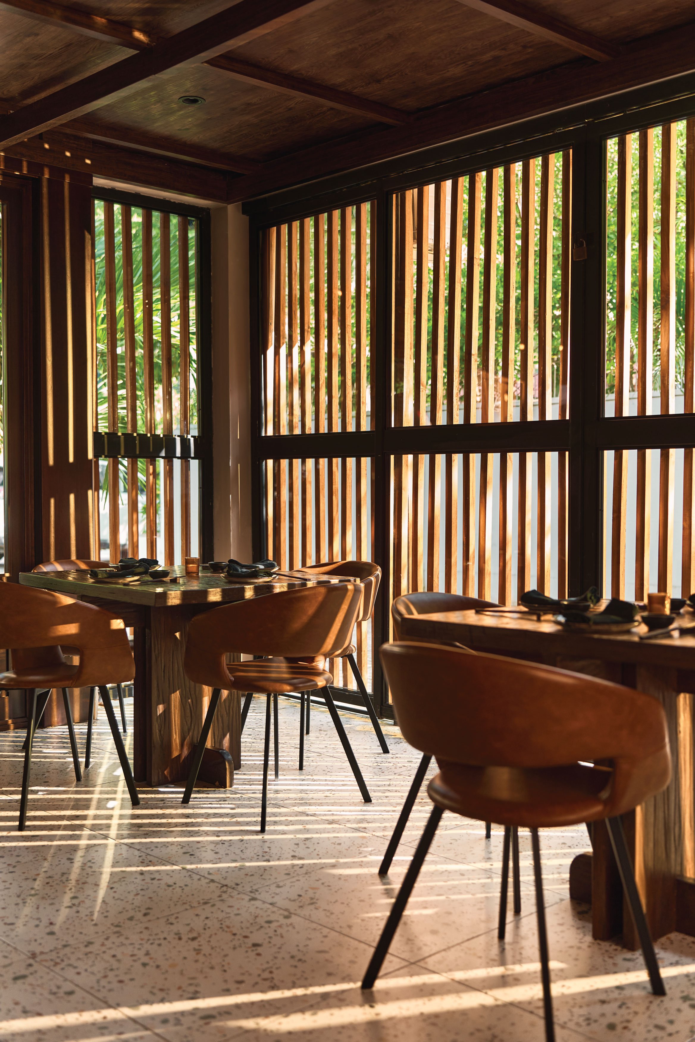 Dining area with leather chairs and round tables behind a wood slat facade, Satori Nosara