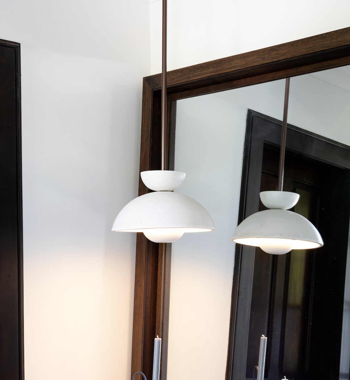 White modern pendant light fixture reflected in a mirror with a wooden frame, mounted on a white wall.