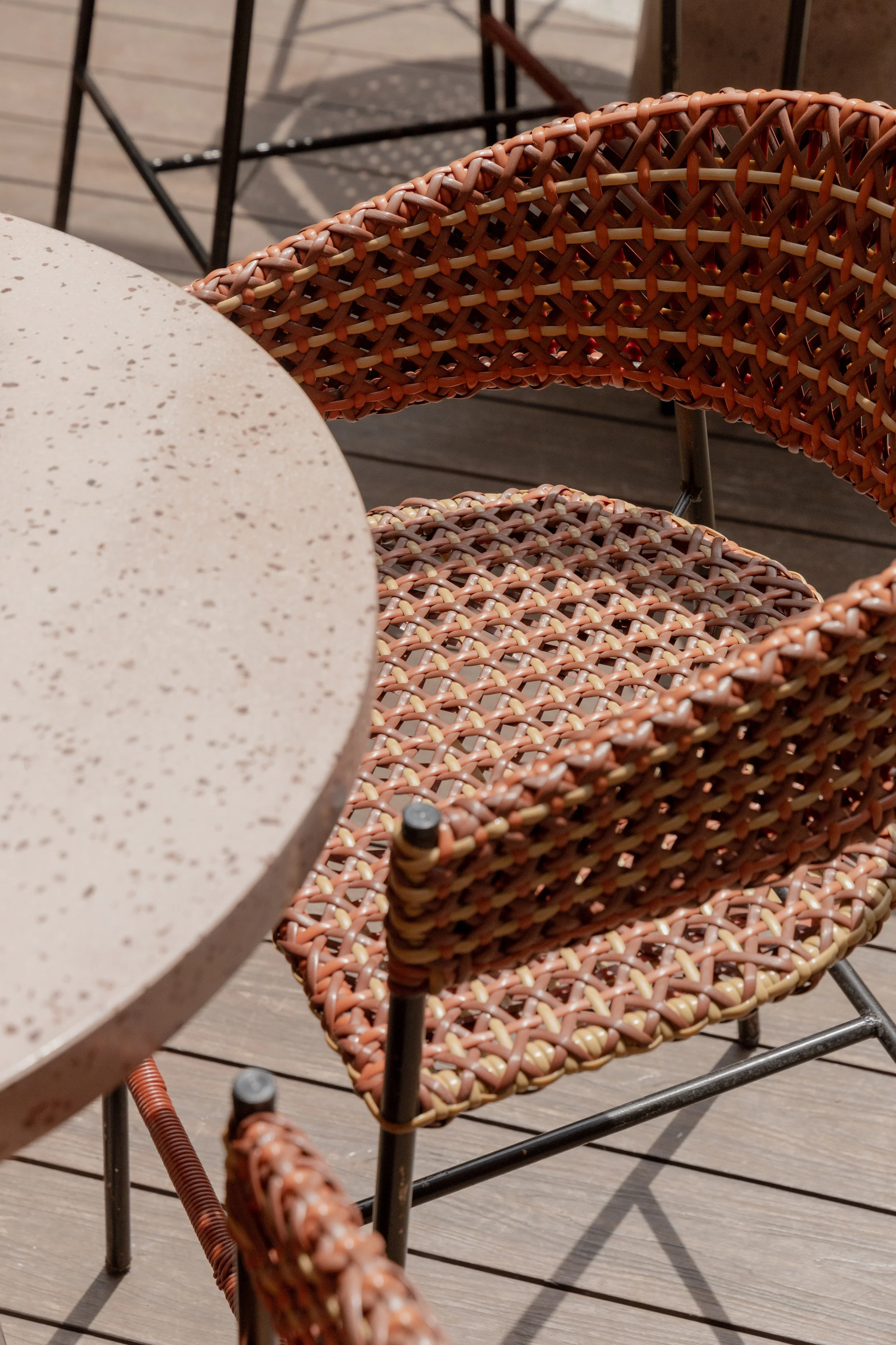 Close-up of outdoor furniture, including a speckled round tabletop and woven rattan chairs on a wooden deck.