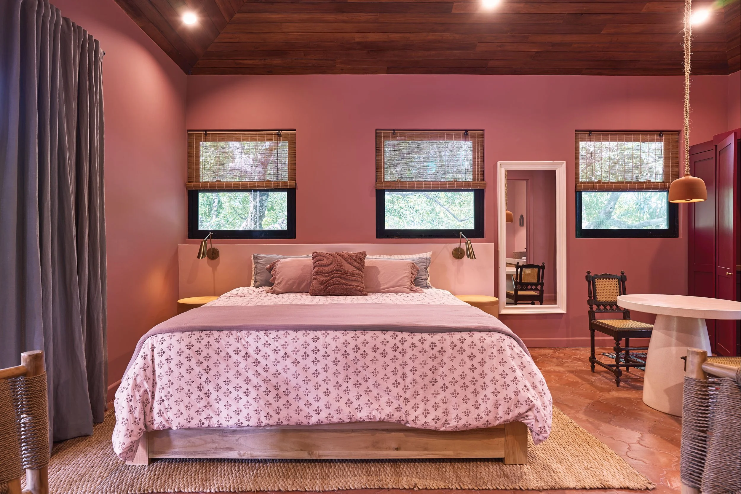 Pink bedroom with patterned bedding, roman shades and a small dining corner