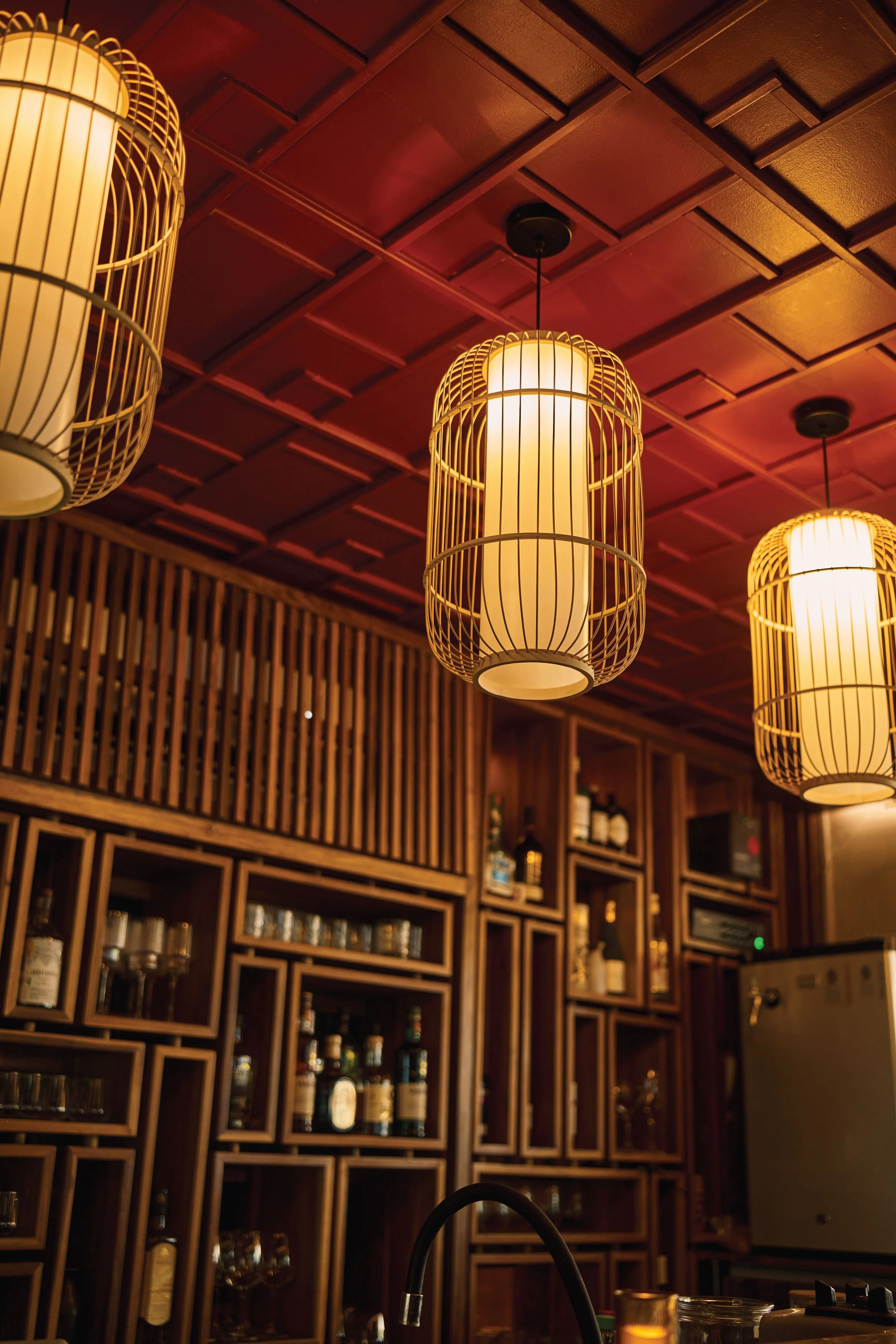 Bamboo lantern pendants over wood slat screens and a bottle wall, Satori