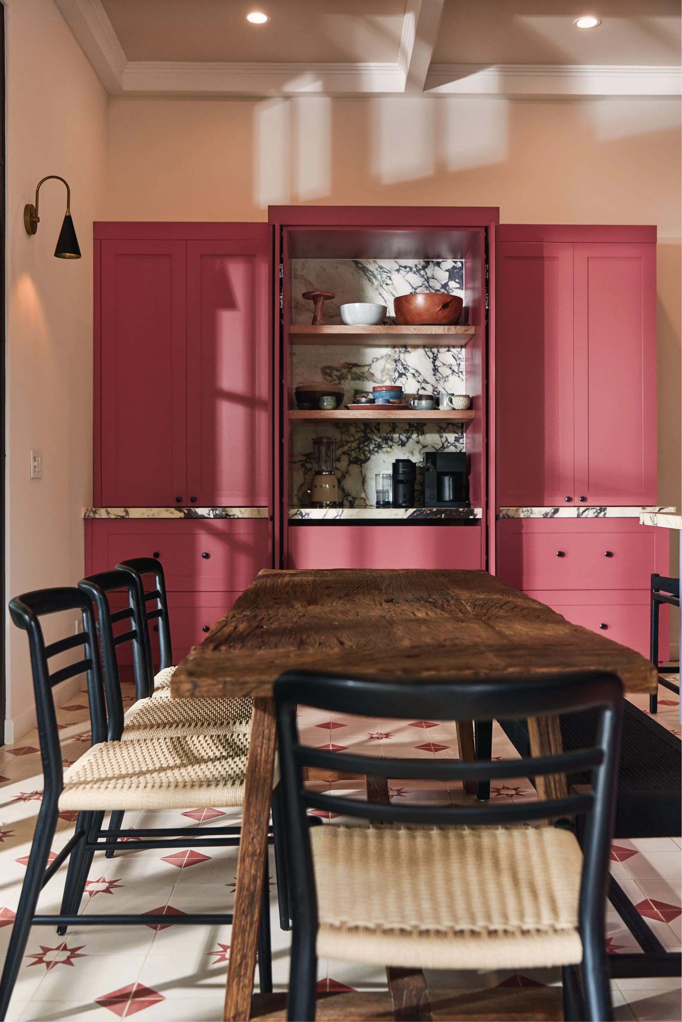 Raspberry-pink kitchen cabinetry with a marble backsplash and a rustic wood table