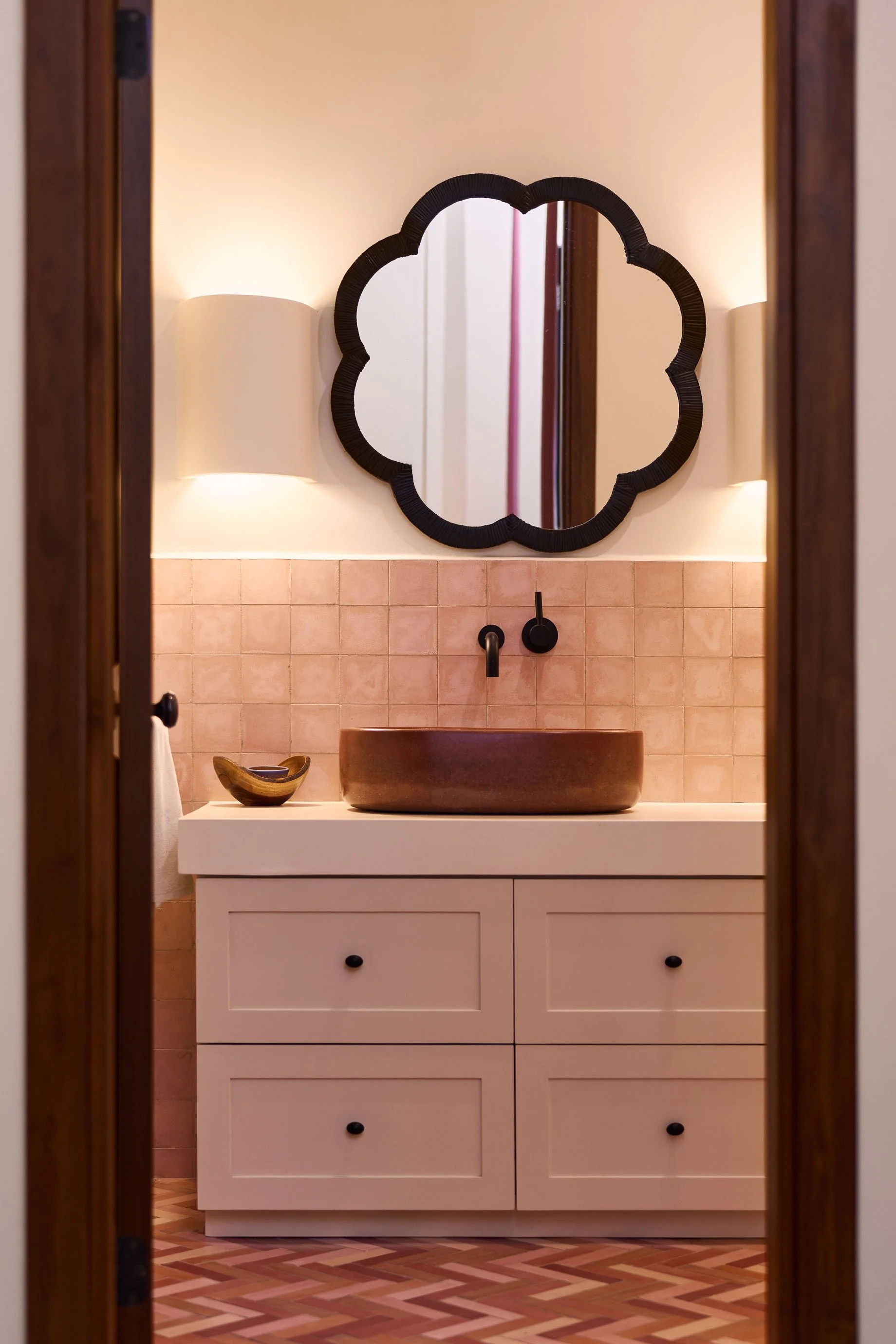 Pink tiled powder room with a scalloped mirror and a copper vessel sink