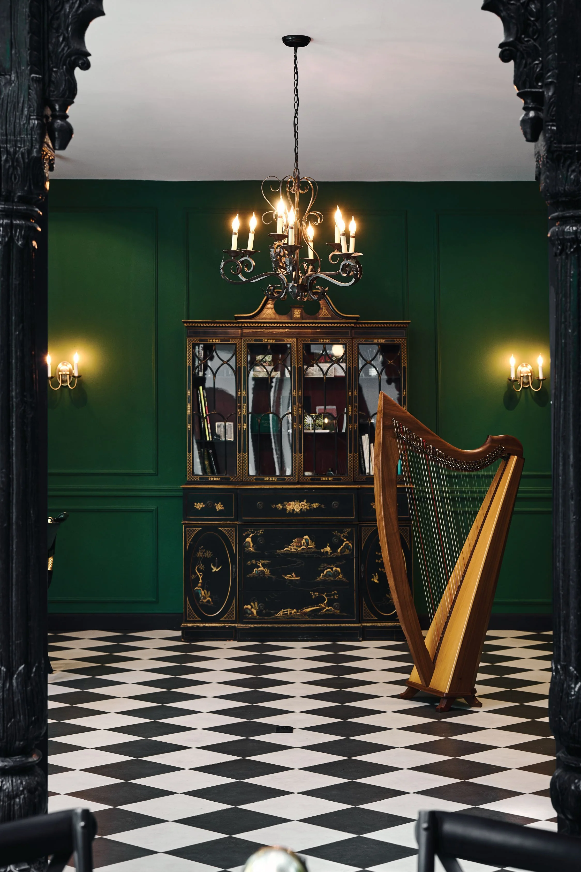 Deep green room with a harp, a chinoiserie cabinet and brass wall sconces, Casa de Malka