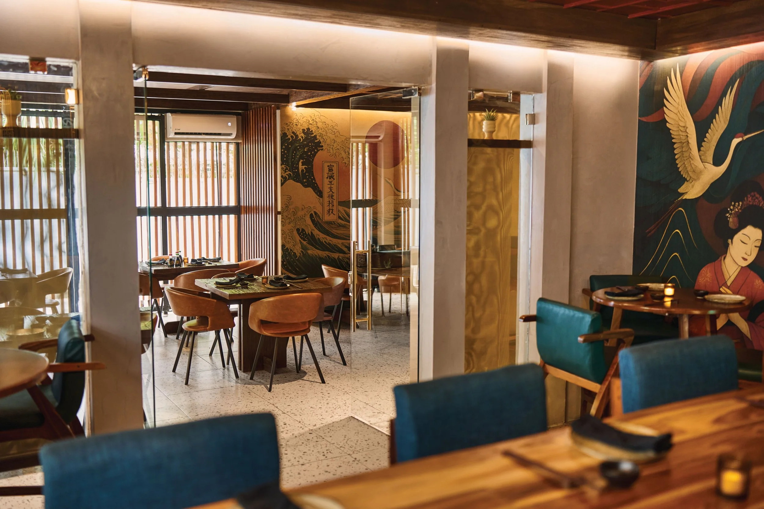 Interior view of a restaurant with wooden and colorful furniture, Asian-inspired wall art, and natural lighting.