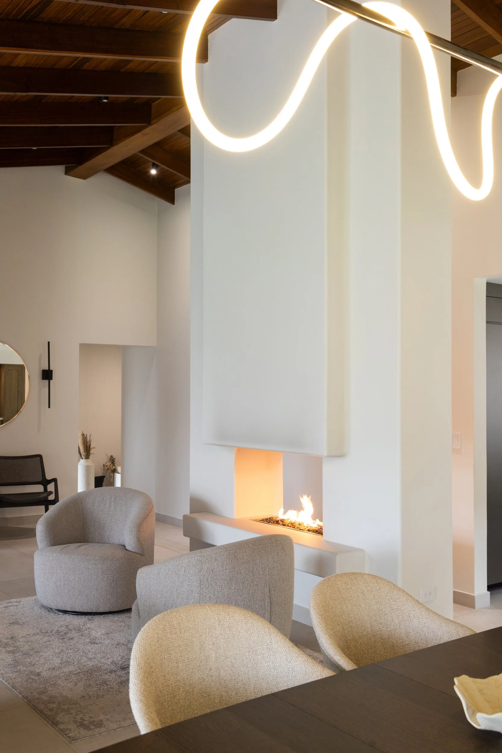 Living room with a white fireplace, beige arm chair sand wood ceiling, a residential interior by Phibra