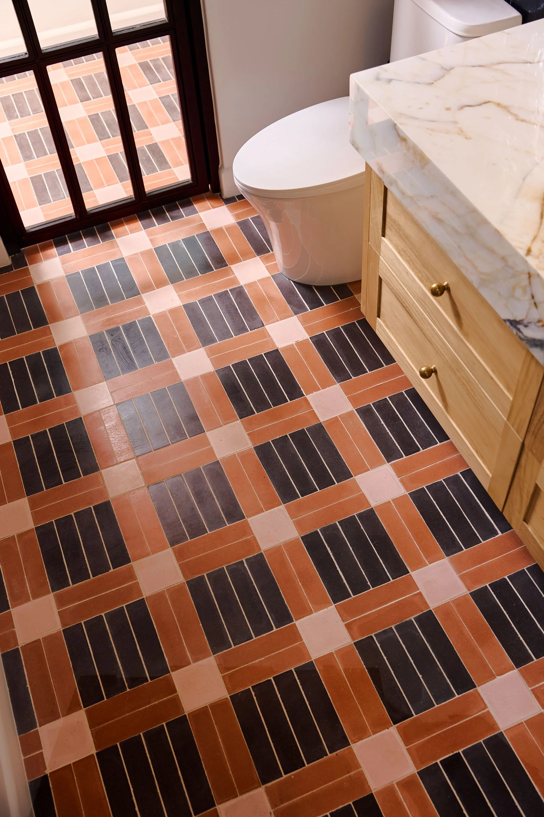 Patterned floor in terracotta, pink and black tiles beside an oak vanity, Casa Ladera