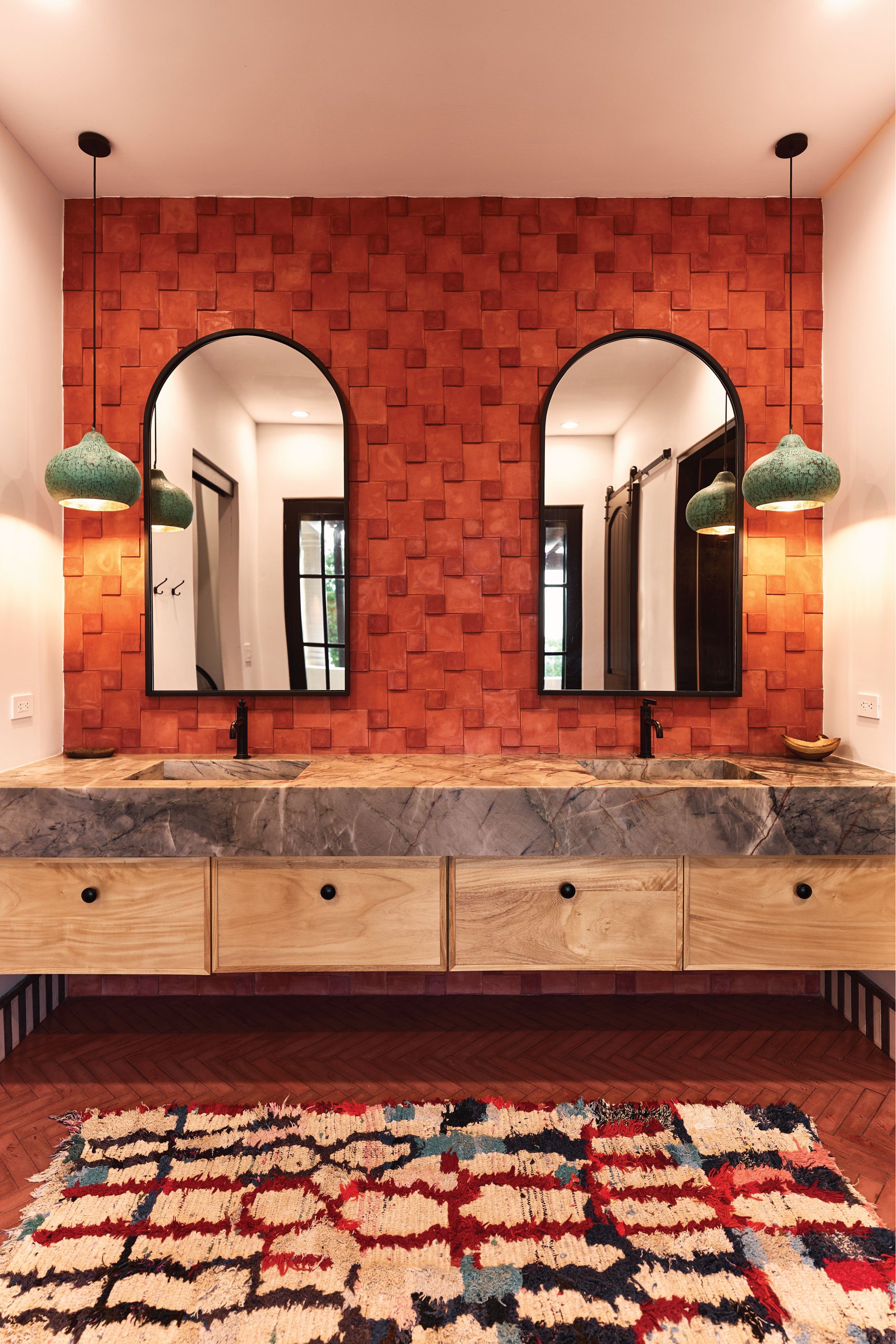 Grey stone double vanity with black mirrors, terracotta 3D tile wall and green pendants