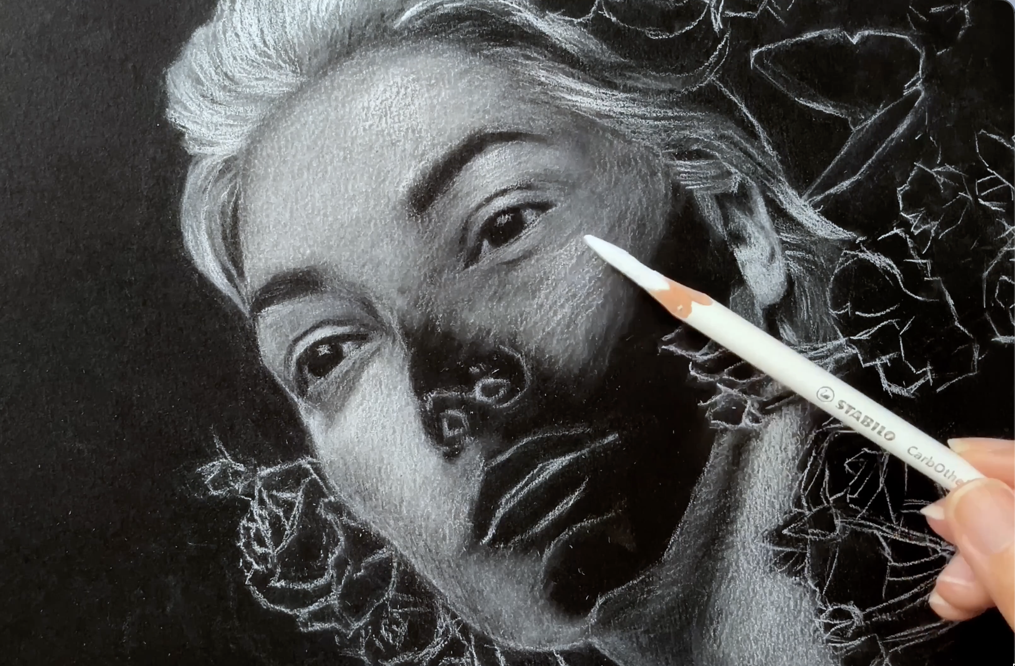 An artist draws a portrait of a woman using white pastel on black paper.