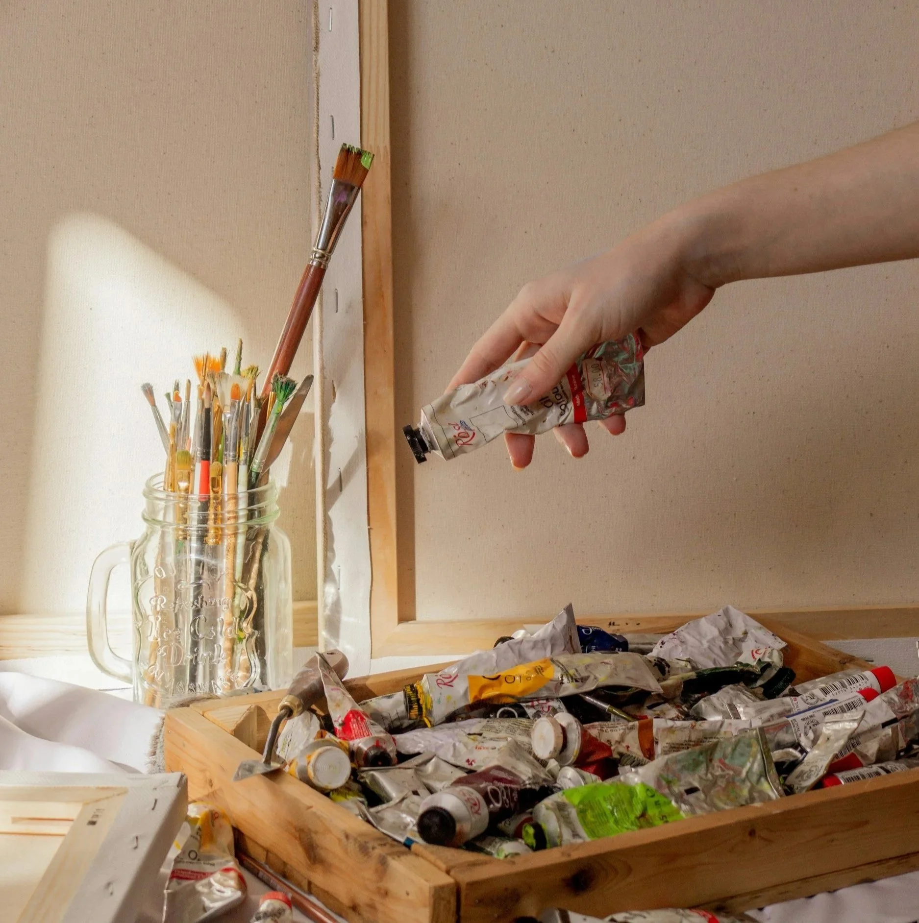 A ceramic mug with black speckles filled with various artist paintbrushes on a table.