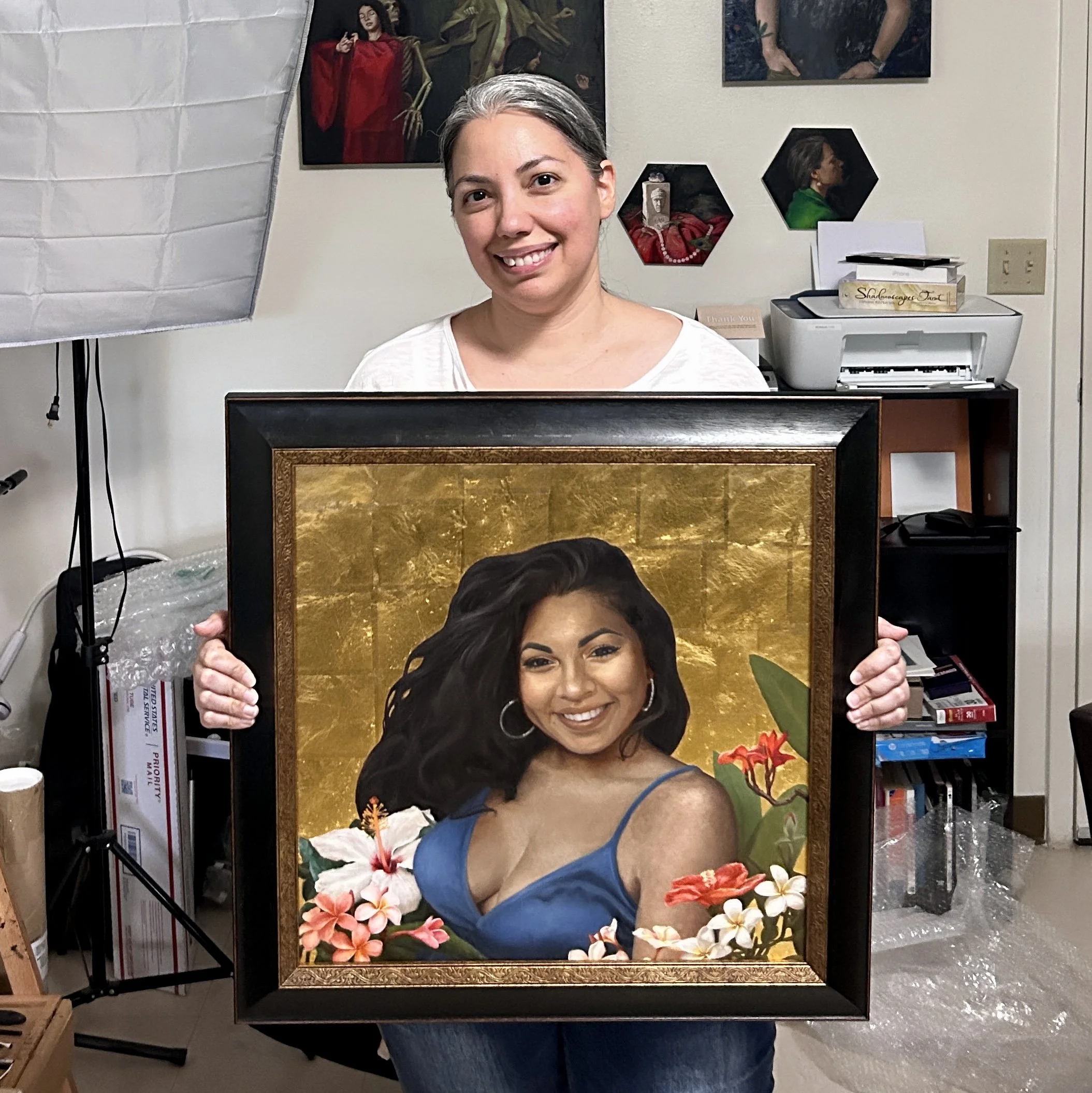 An artist holds a commissioned painting of a woman surrounded by flowers and gold leaf.