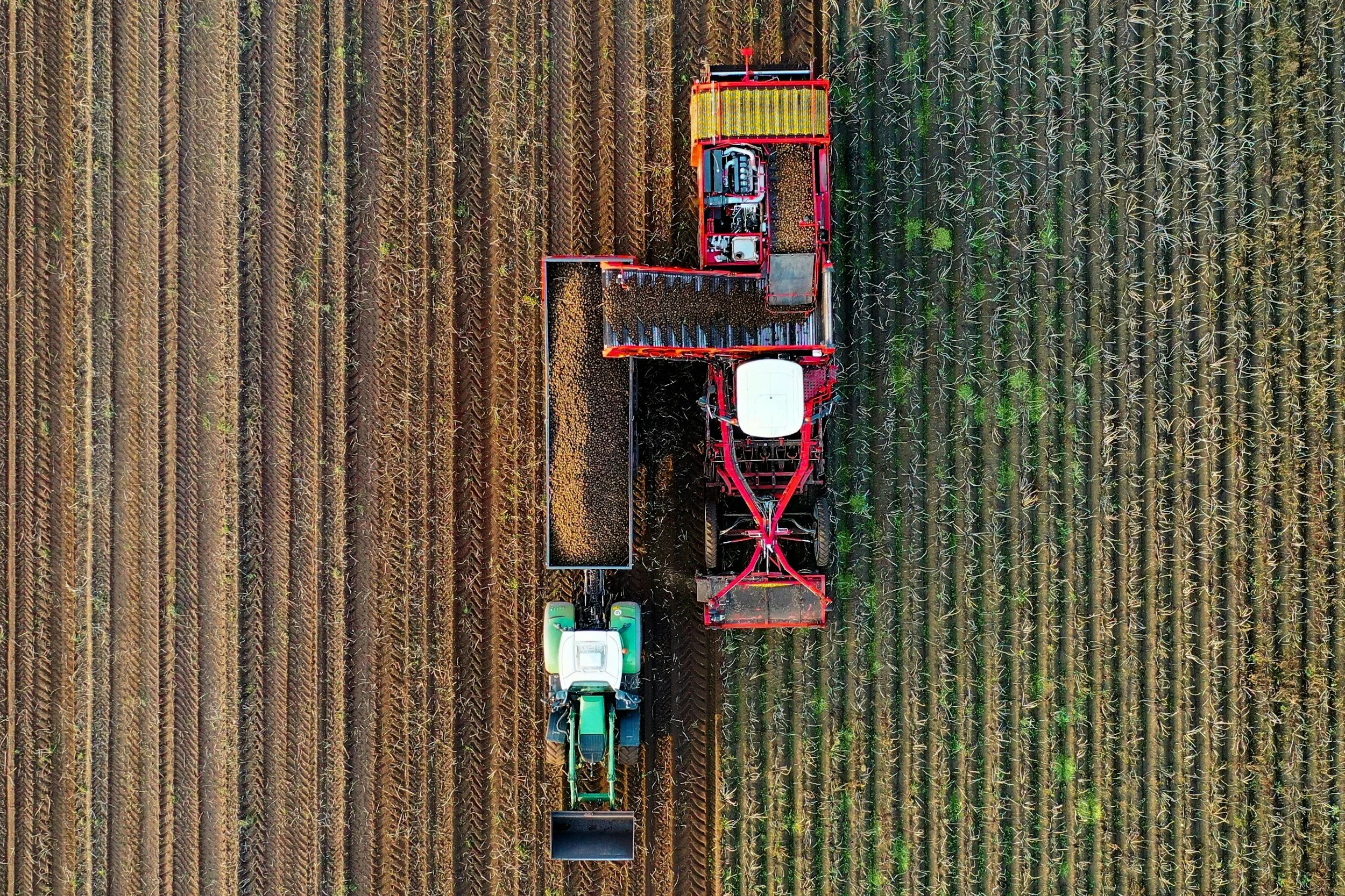 An aerial view of a tractor and a harvesting machine working in a field of crops.