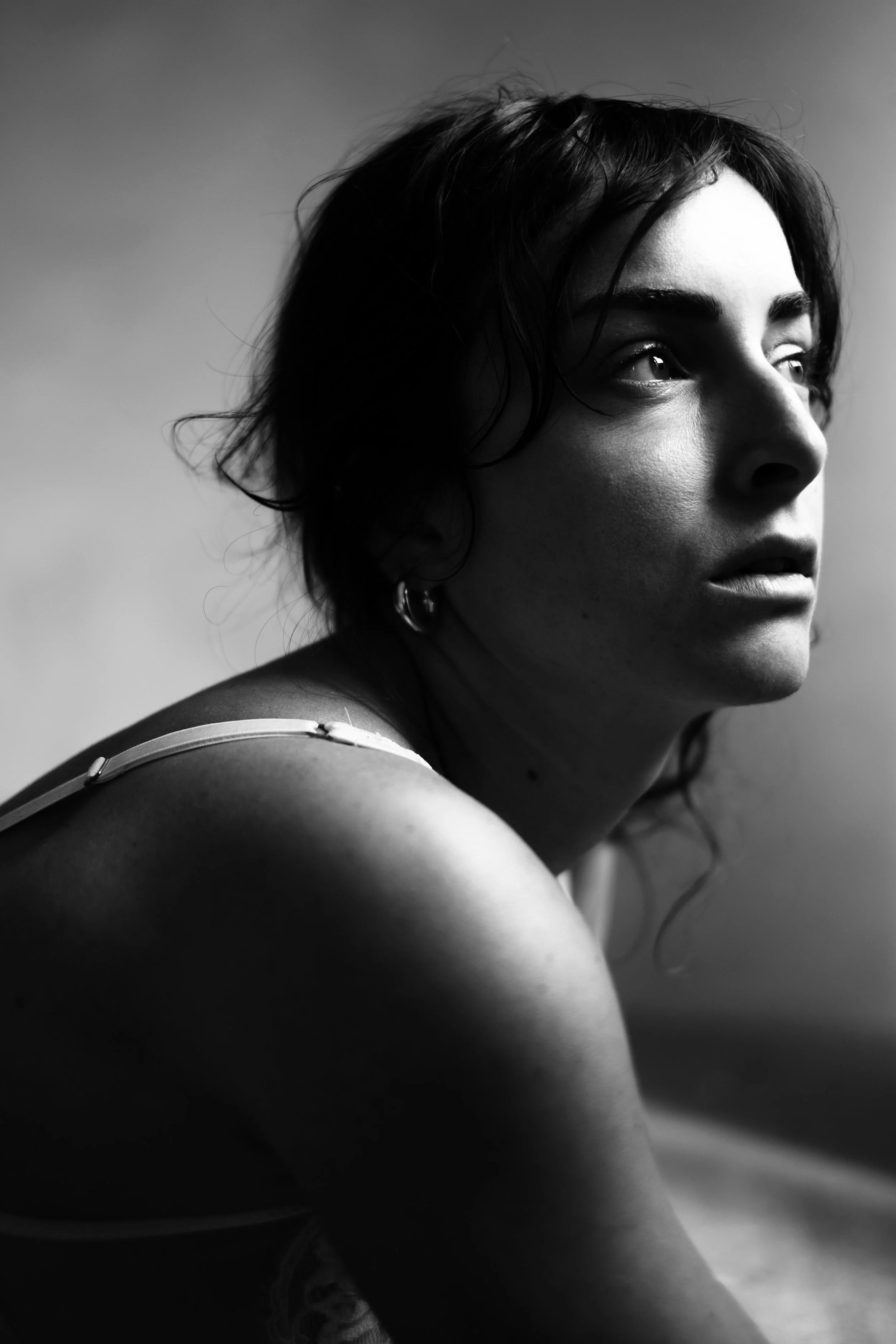A black and white photo of a woman with short, wavy hair and hoop earrings looking to the right with natural light highlighting her face.