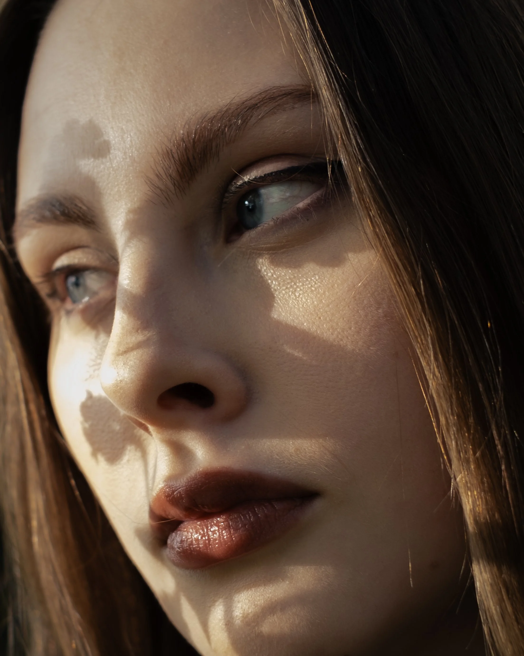 Close-up of a woman's face showing part of her eye, nose, and lips with dark hair falling over her face.