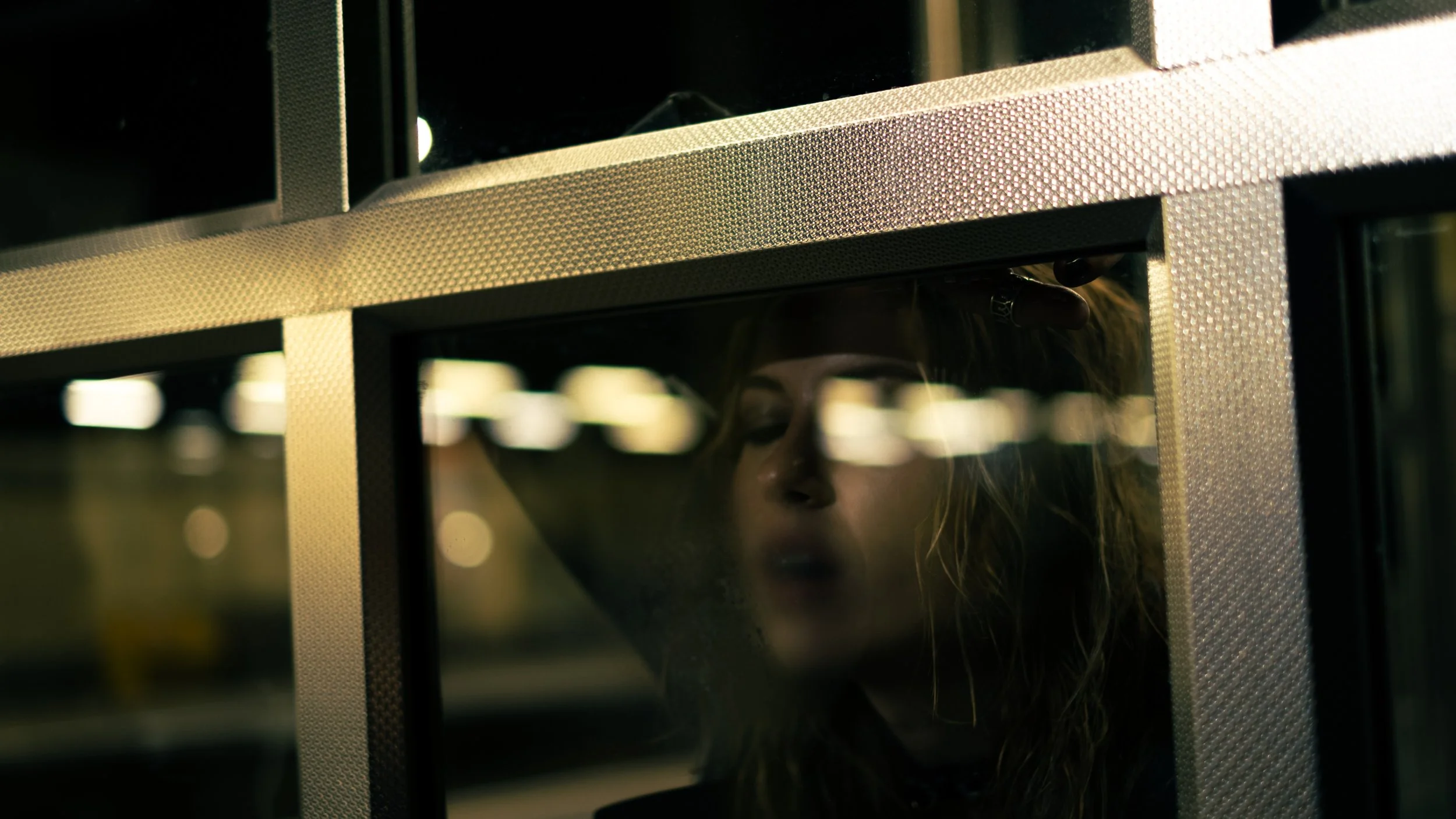 Close-up of a person looking through a glass window in a metallic structure, with only their face partially visible.