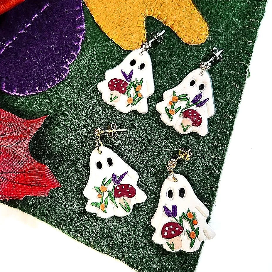 White sheet ghost earrings with a mushroom theme lying on a fall colored background