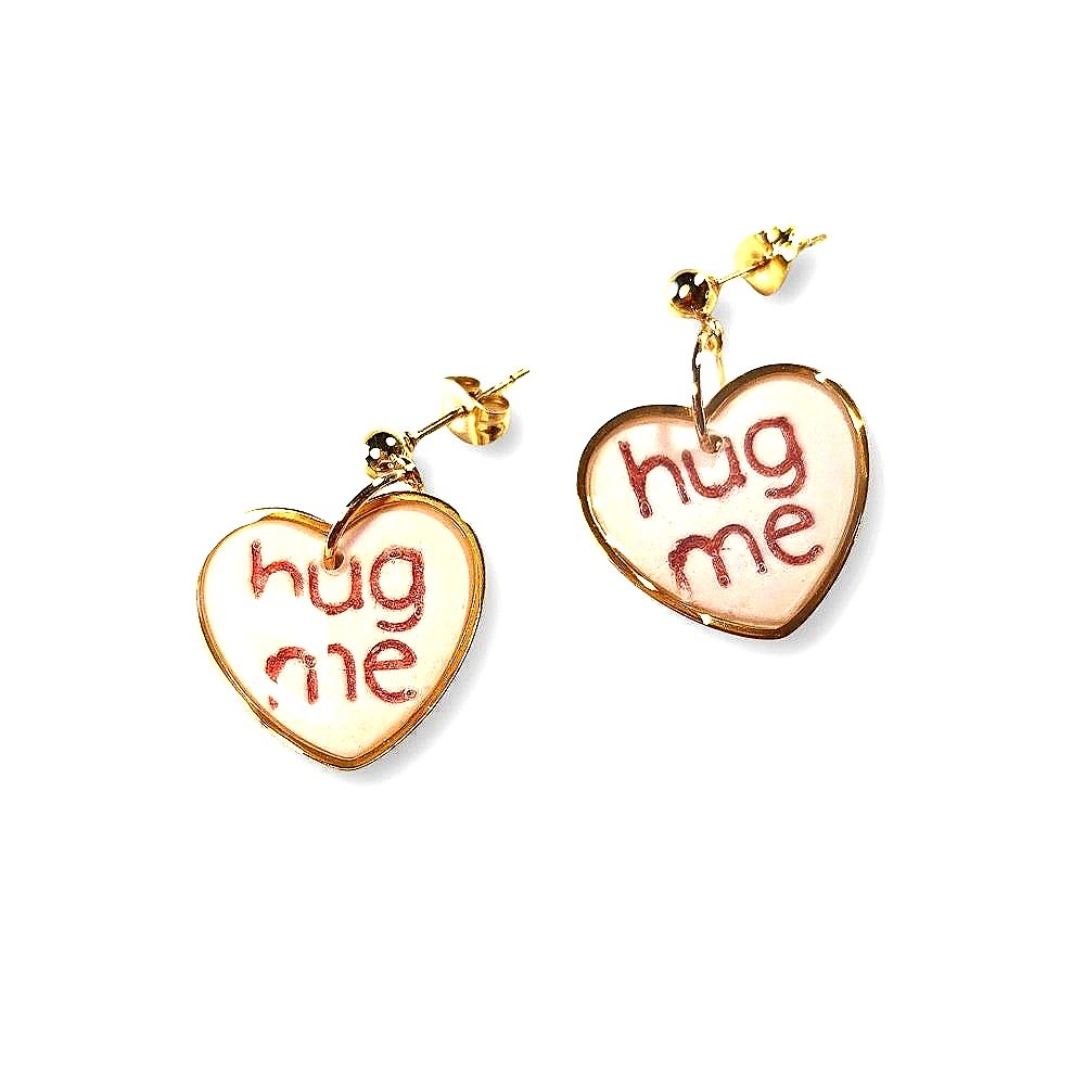 white conversation heart dangle earrings with gold rim and red lettering saying: ' Hug Me'