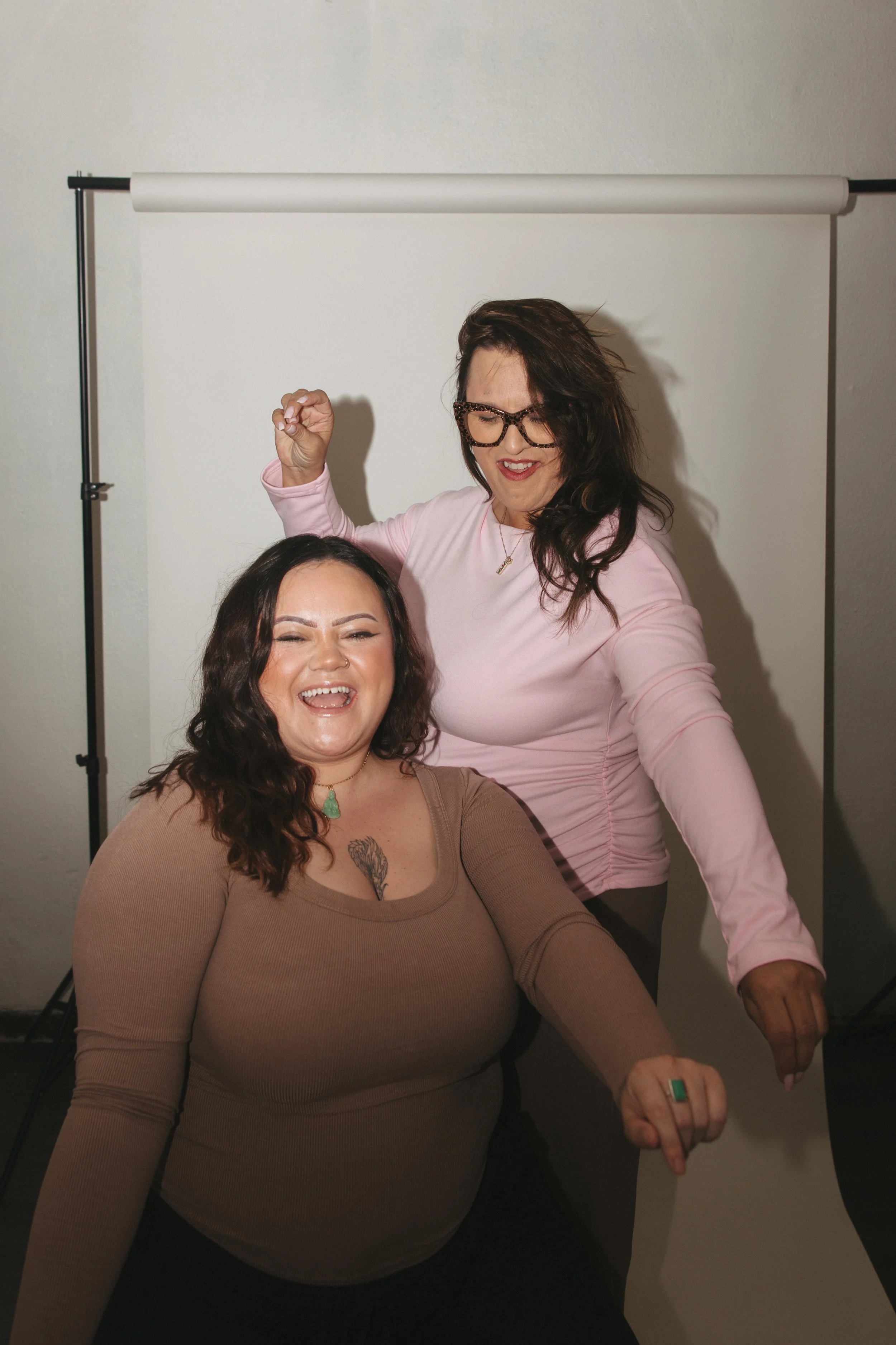 Two women laughing while creating a safe and supportive space for women to come and heal, are posing happily, showing joyful expressions.