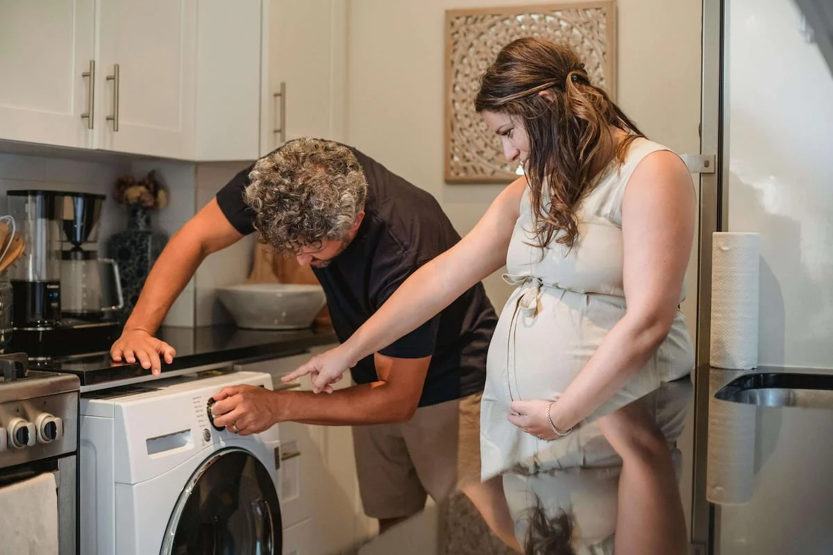 A pregnant woman gives instructions to her partner in the kitchen. Representing the hidden mental load women face in family roles. Counseling for women across Texas, including Houston and Dallas, can help support mental health through online therapy.
