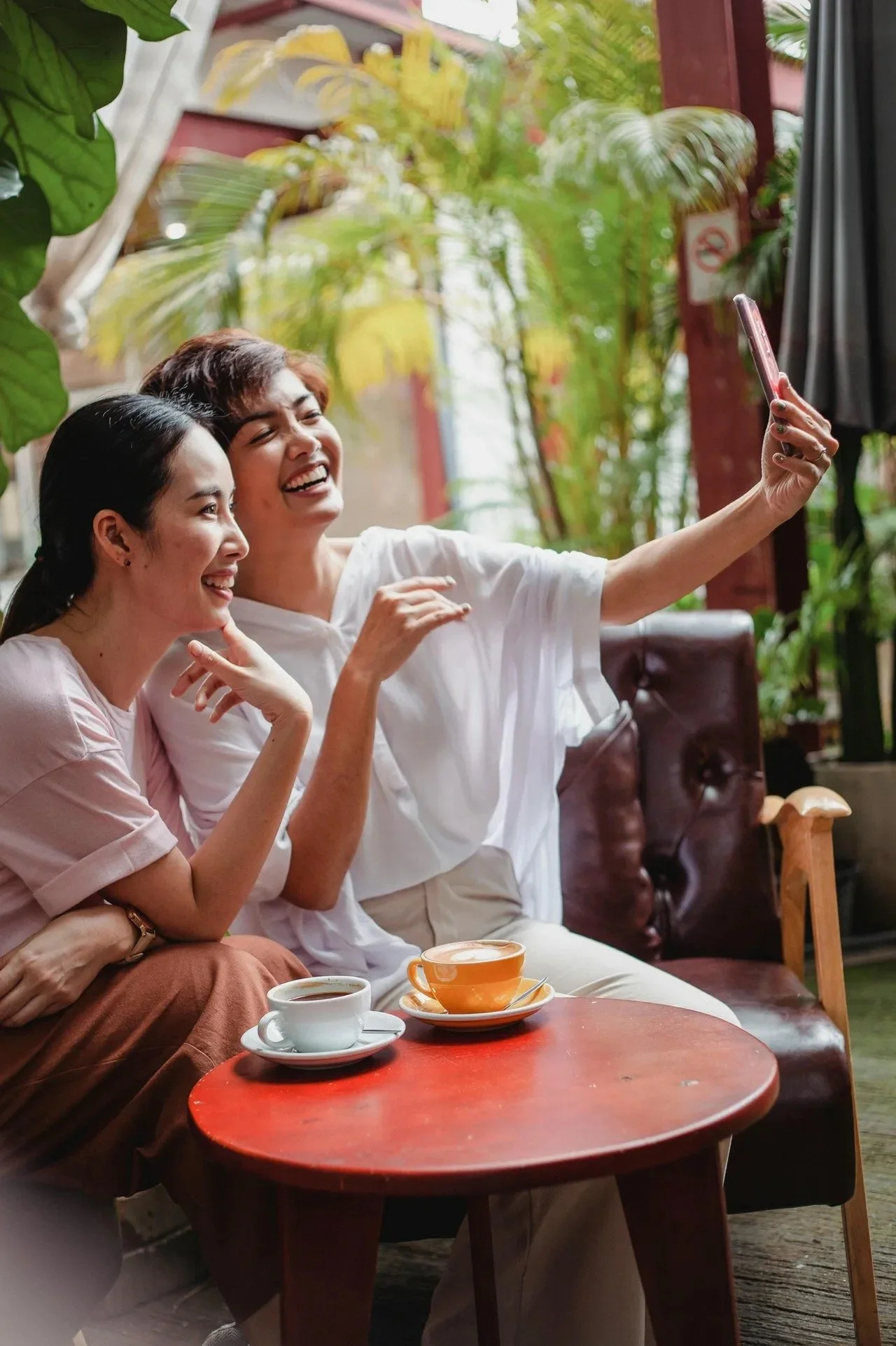Two Asian women friends, smiling while taking a selfie. Symbolizing genuine connections, lighthearted fun, and mutual support, also available through online counseling for women, offered by Latina therapist in Texas