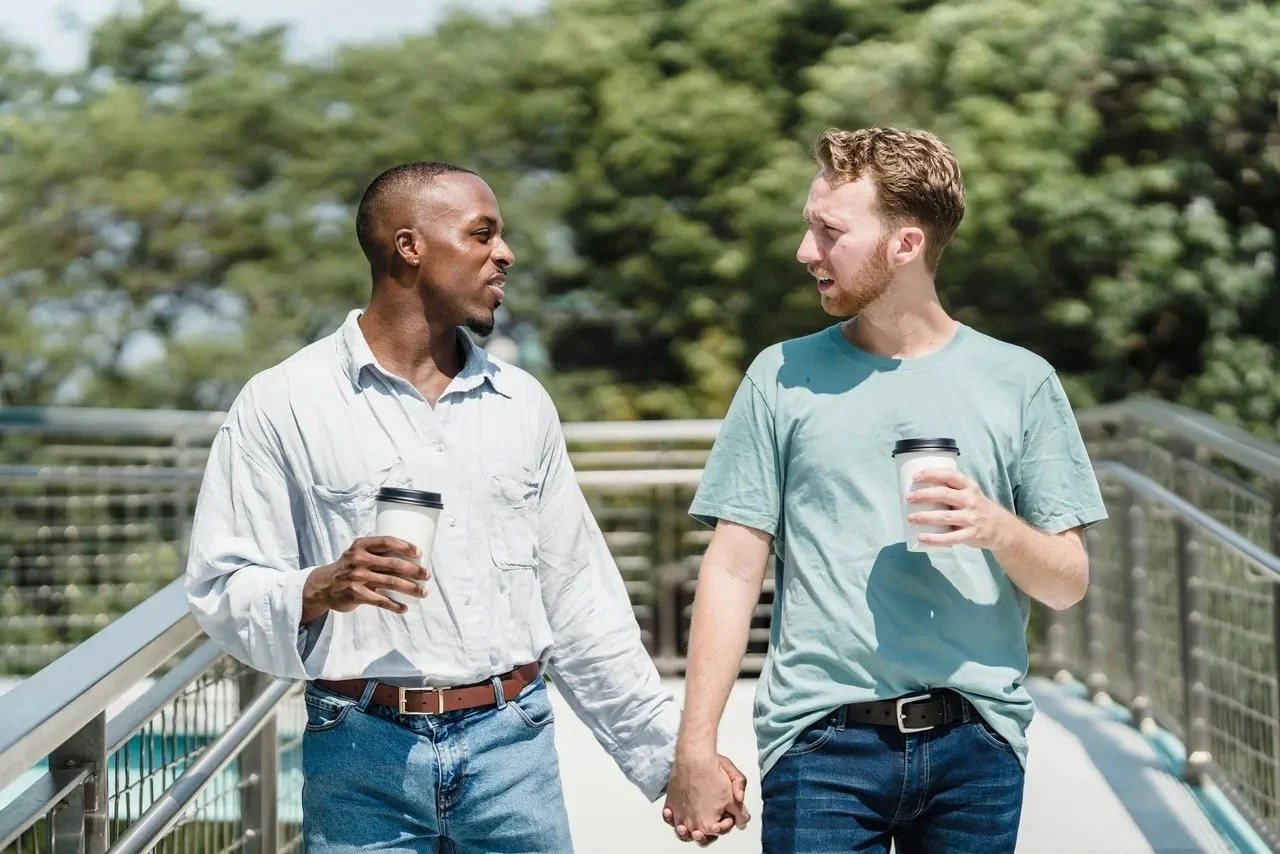 Gay couple holding hands, walking, and talking while holding a cup of coffee