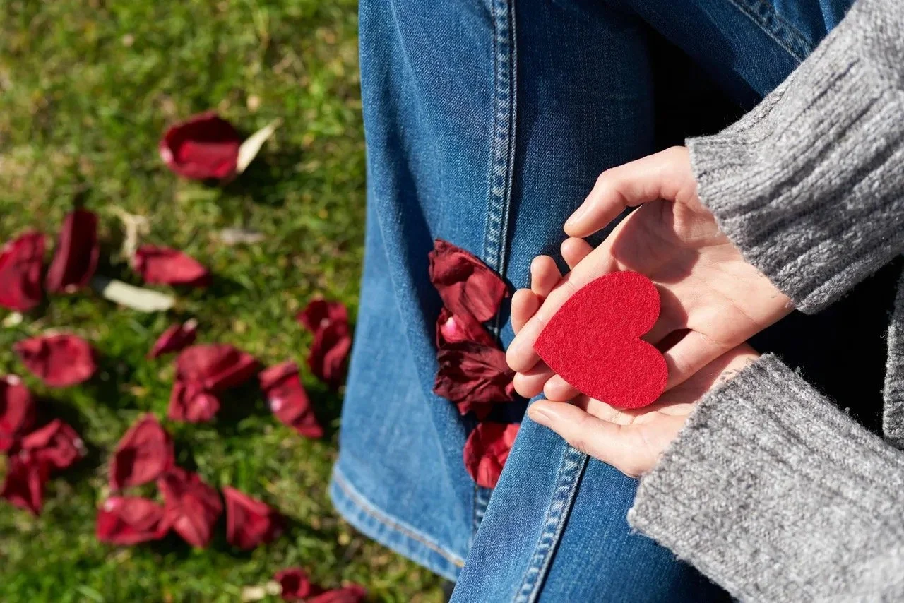 Woman sitting on grass, holding red heart, symbolizing courage and care of deciding to start online therapy for one's healing and personal growth. Available through online therapy for women at Graceful Mind Therapy, across Texas, New Mexico, Arizona