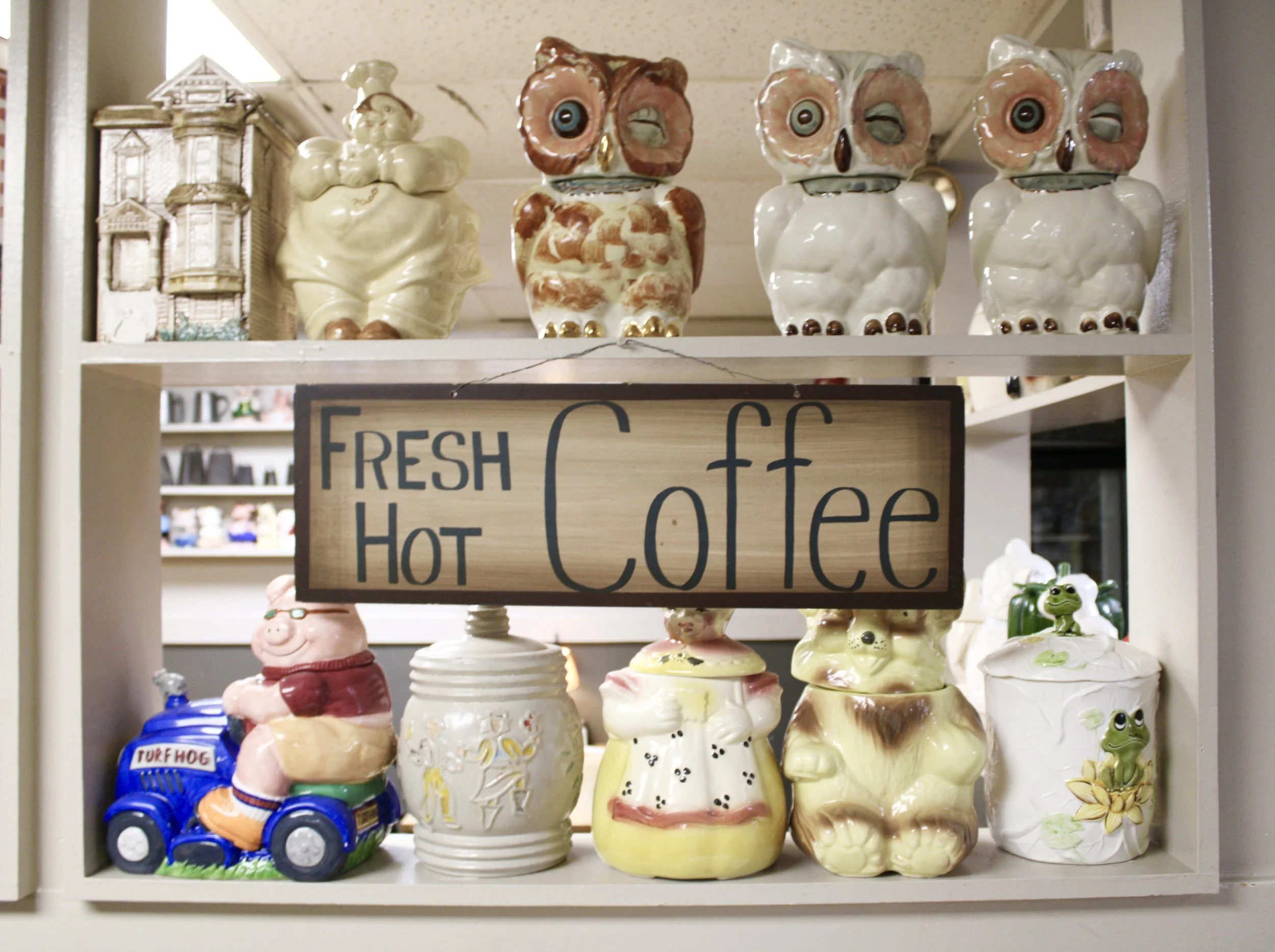 Collected cookie jars on wooden shelves with a “Fresh Hot Coffee” sign at Country Deli in Gradyville, PA
