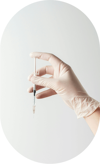 A gloved hand holding a syringe with liquid inside against a plain background.