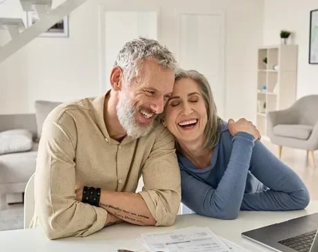 A happy elderly man and woman laughing together at a table in a bright living room.