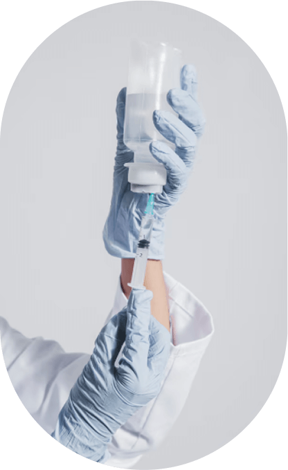 A medical professional's hands in blue gloves drawing liquid from a large vial with a syringe.