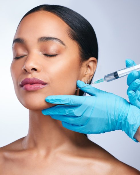 Close-up of a woman receiving a facial injection with her eyes closed, while a medical professional wearing blue gloves administers the treatment.