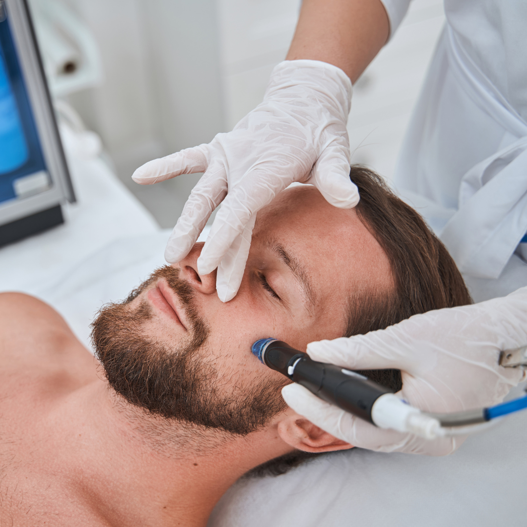 A man receives a medical or dental treatment, lying on a bed, with a healthcare professional holding a device near his eye, wearing gloves.