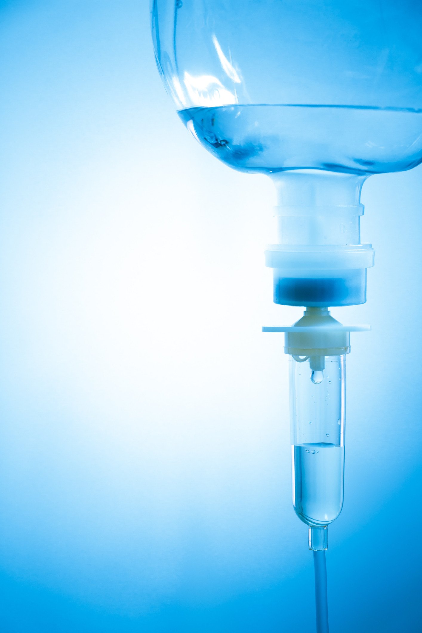 Close-up of a medical IV drip bag filled with clear liquid, hanging against a light blue background.