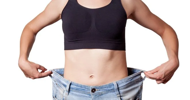 Person wearing a black sports bra and loose denim jeans showing a significant weight loss.