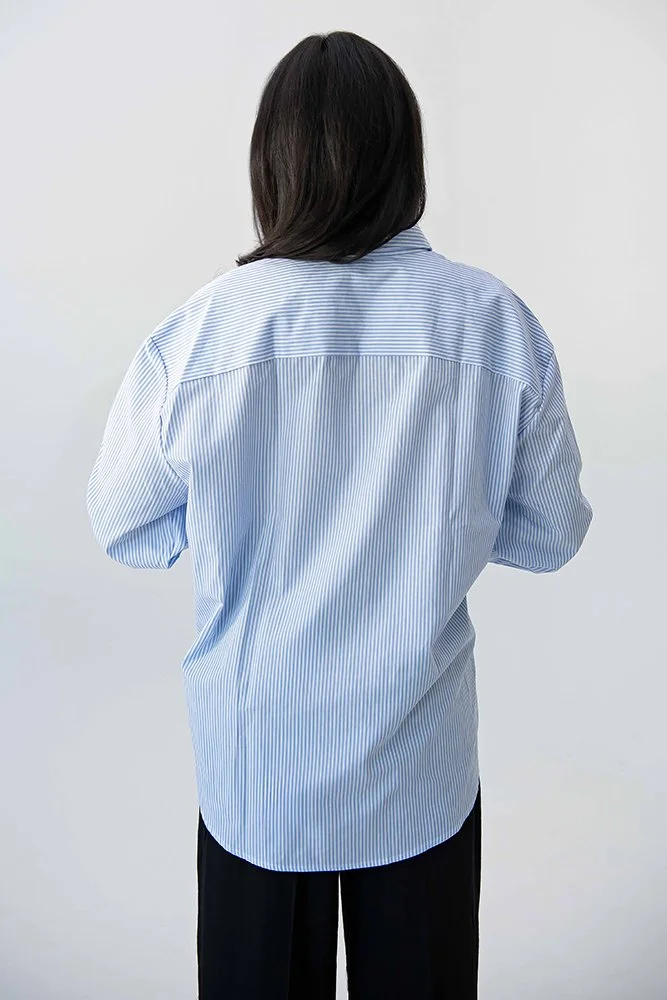 Rückansicht eines hellblau-weiss gestreiften, oversized Unisex-Hemds aus Baumwolle – klassisches Design mit modernem lässigem Schnitt.