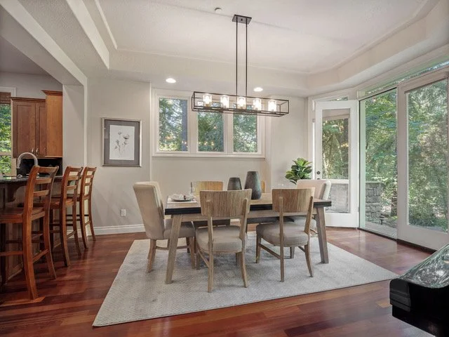 Dining room with a rectangular dining table, six chairs, a modern chandelier, large windows, and glass doors leading outside.