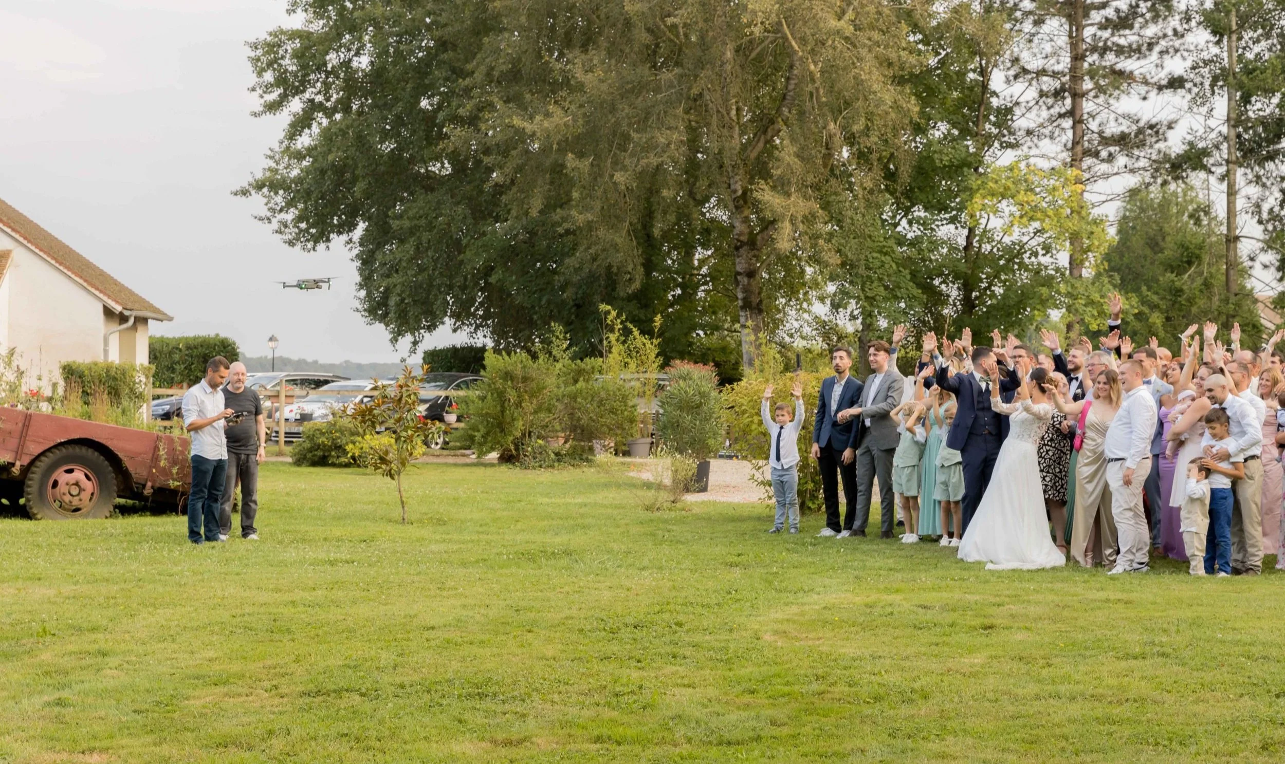 Cérémonie de mariage en plein air avec la mariée, le marié et de nombreux invités applaudissant, sous de grands arbres.
