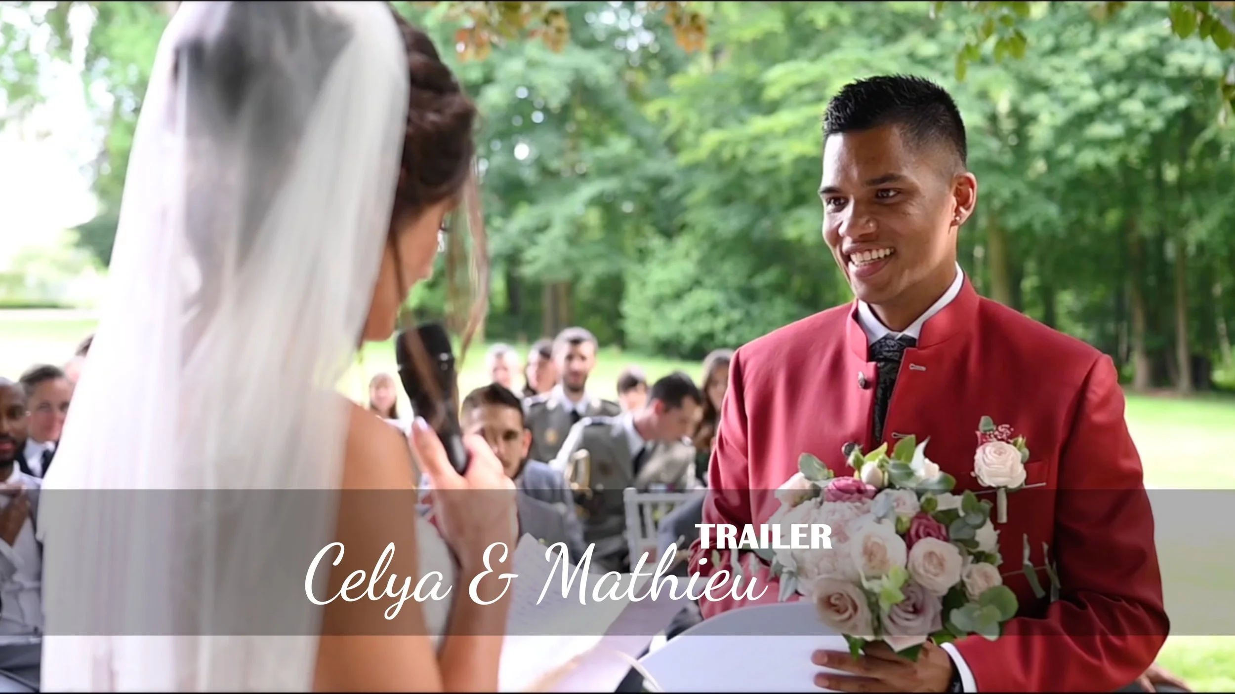 Un homme avec un costume rouge et une femme en robe de mariée échangeant leurs vœux lors d'un mariage en plein air.