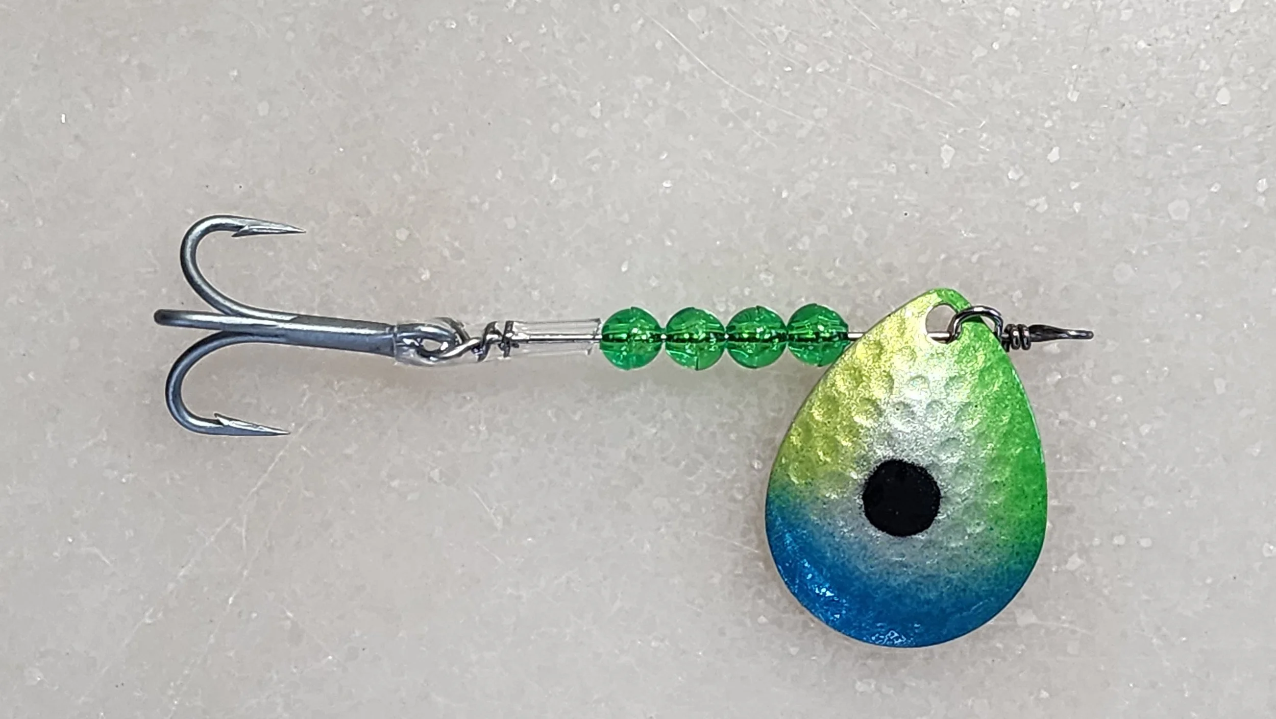 Fishing lure with a metal treble hook, green beads, and a teardrop-shaped painted eye with a black center, green and blue colors.