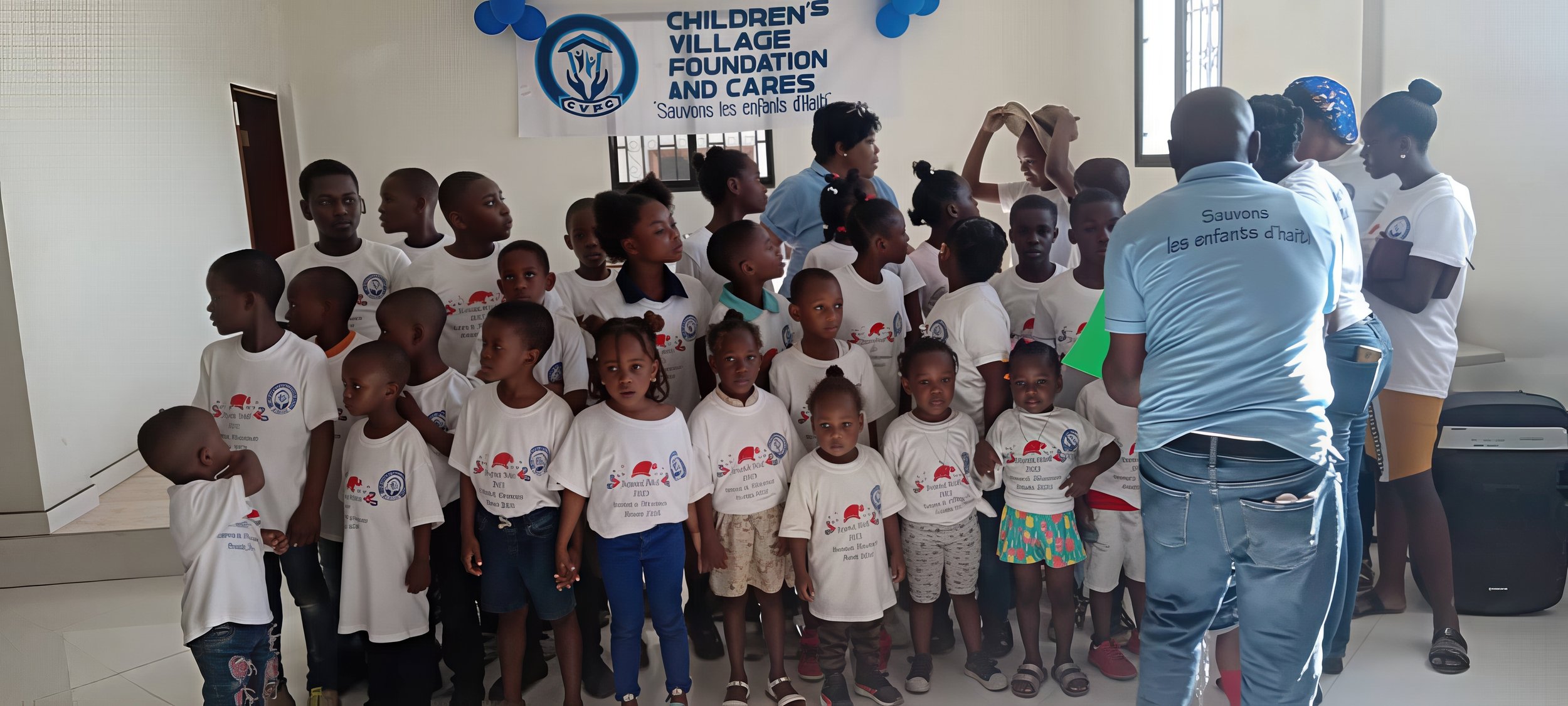 Children participating in a community event organized by the Children's Village Foundation and Cares, indoors with banners and staff members.
