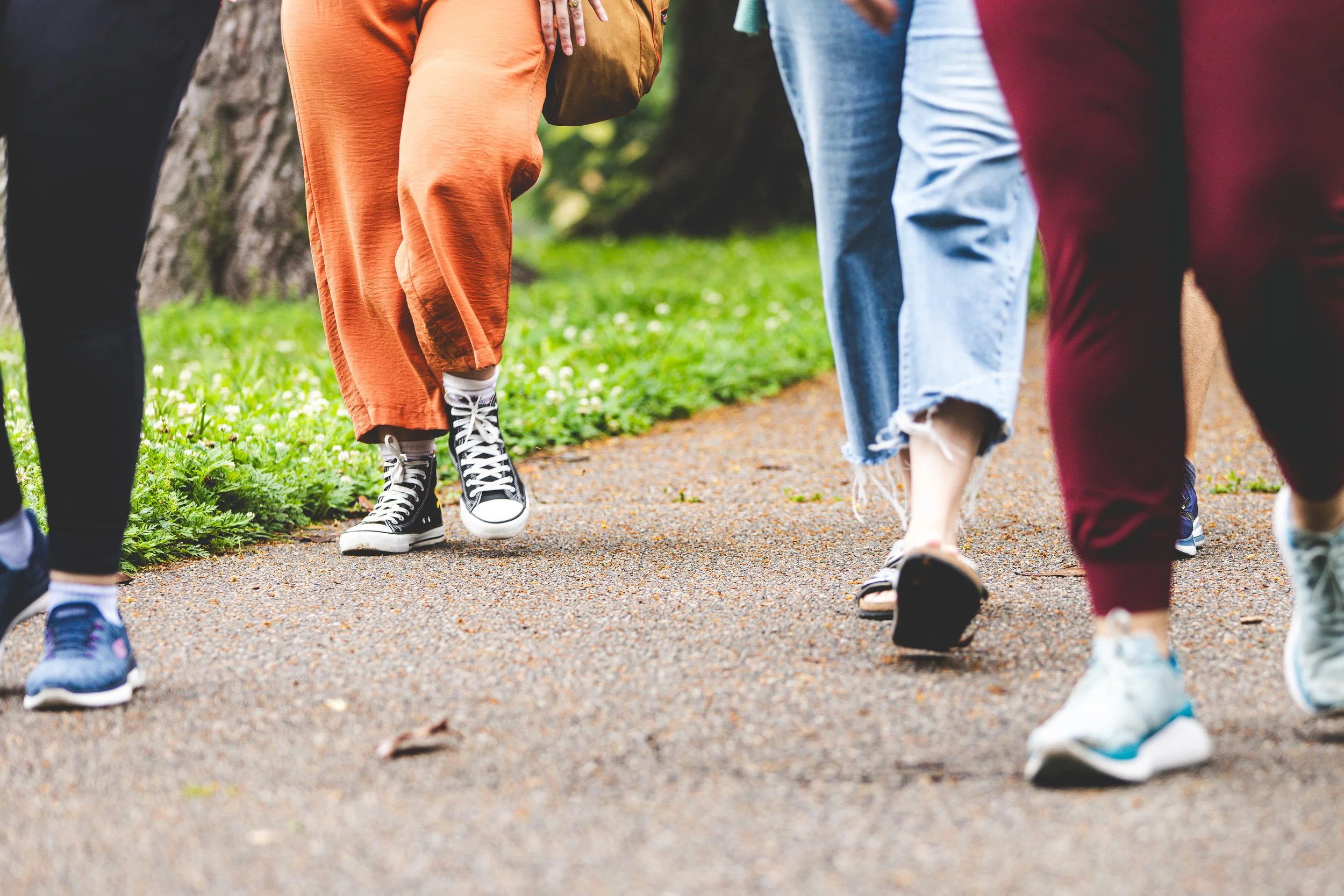People walking on a dirt path in a park, wearing casual clothing and sneakers.