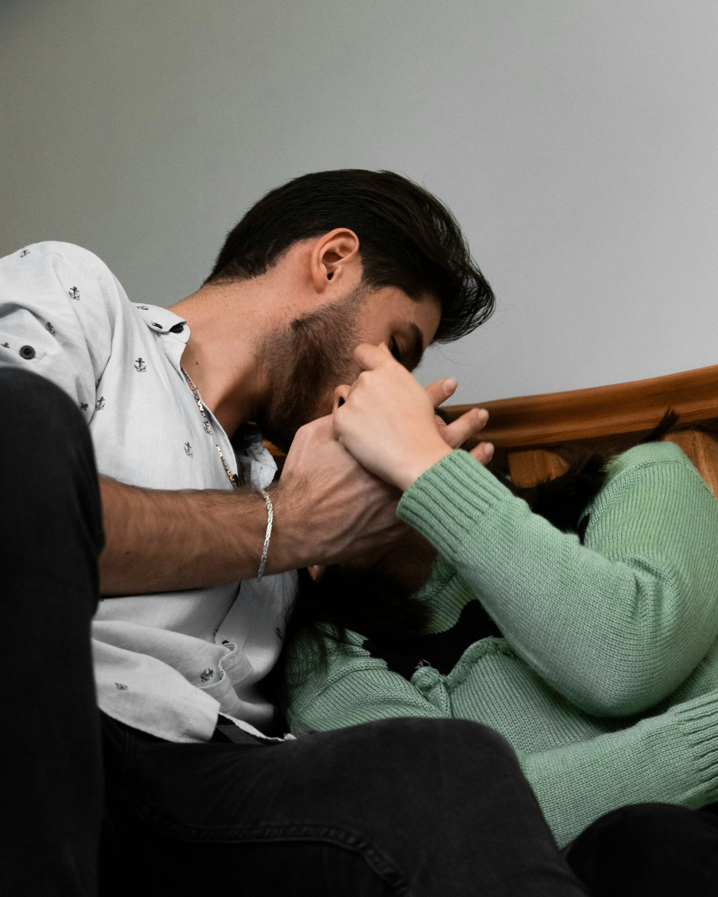 A woman with curly hair kisses a smiling man on the cheek indoors.