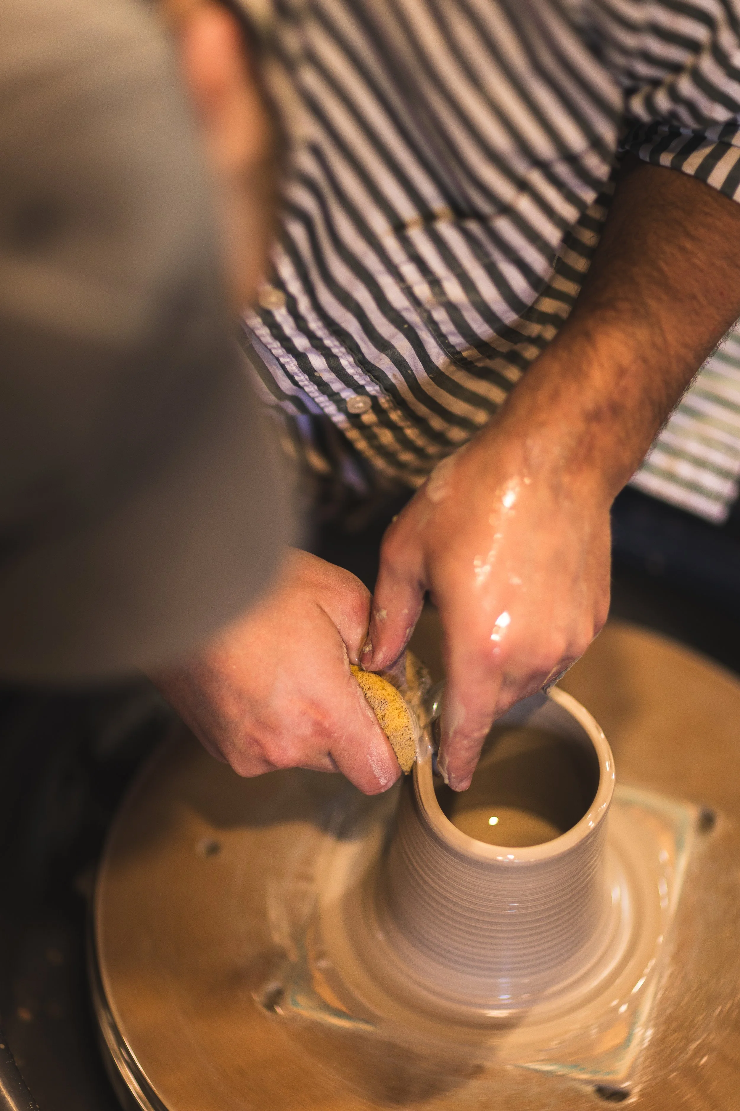 Person shaping a ceramic vase on a pottery wheel.