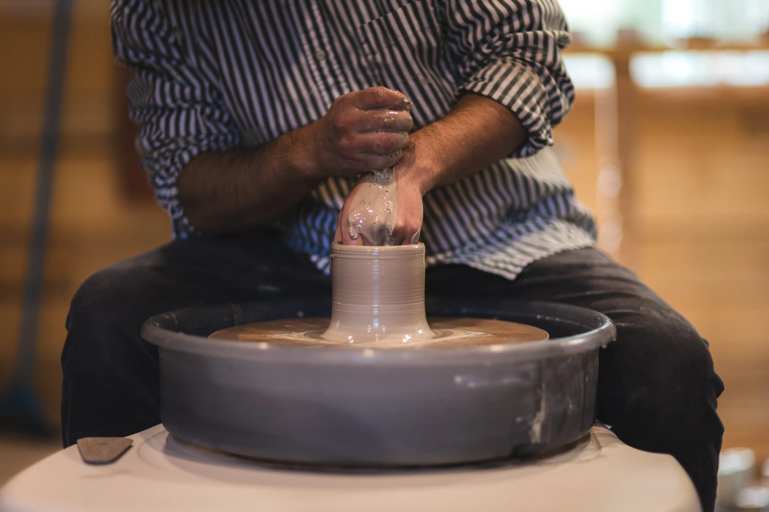 Person shaping clay on a pottery wheel in a studio.