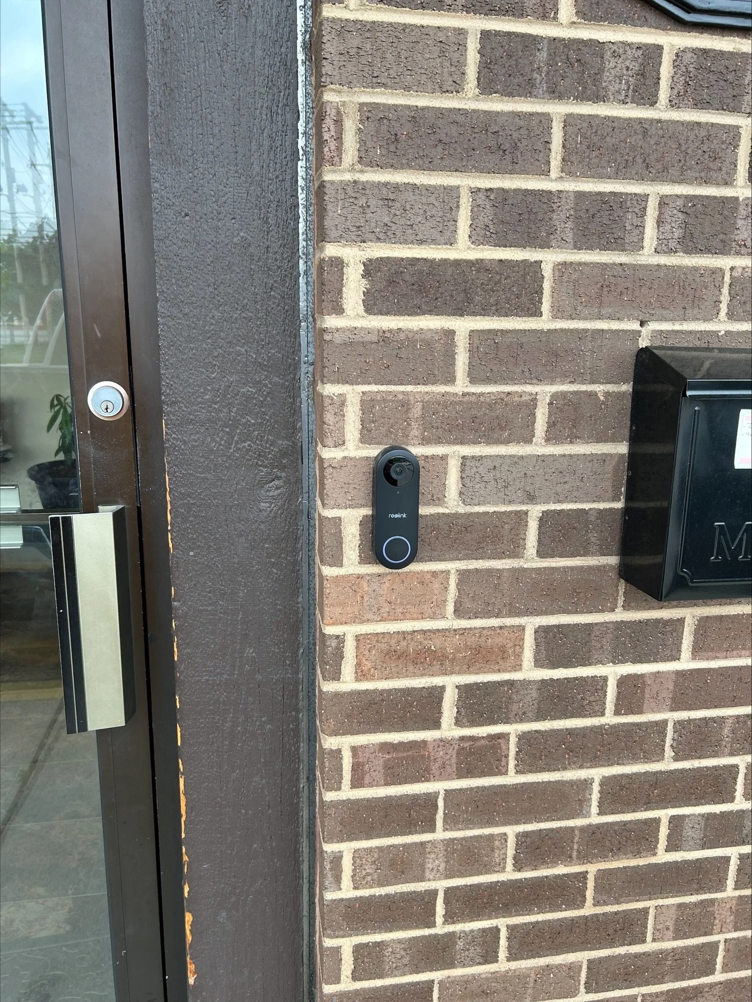 Close-up of an outdoor security camera mounted on a brick wall next to a glass door.