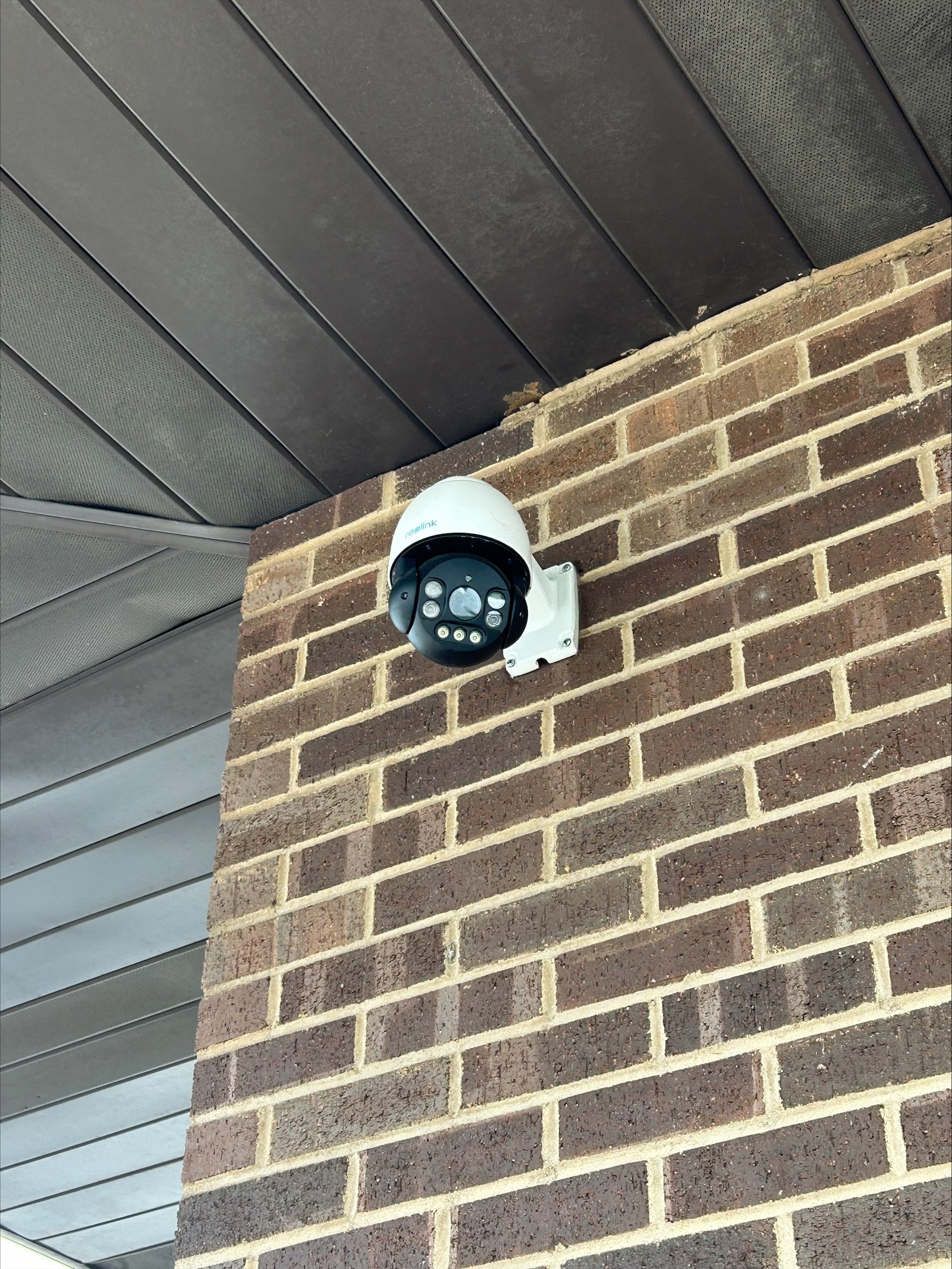 A security camera mounted on a brick wall under a roof.