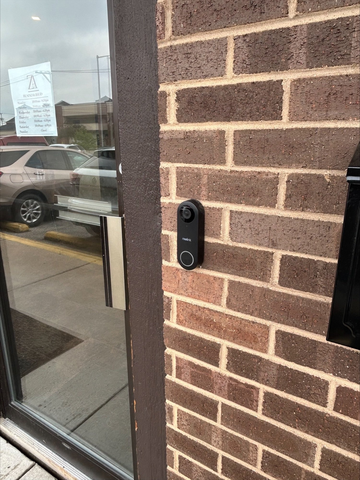 Outside view of a glass door with a security camera mounted on a brick wall next to it.